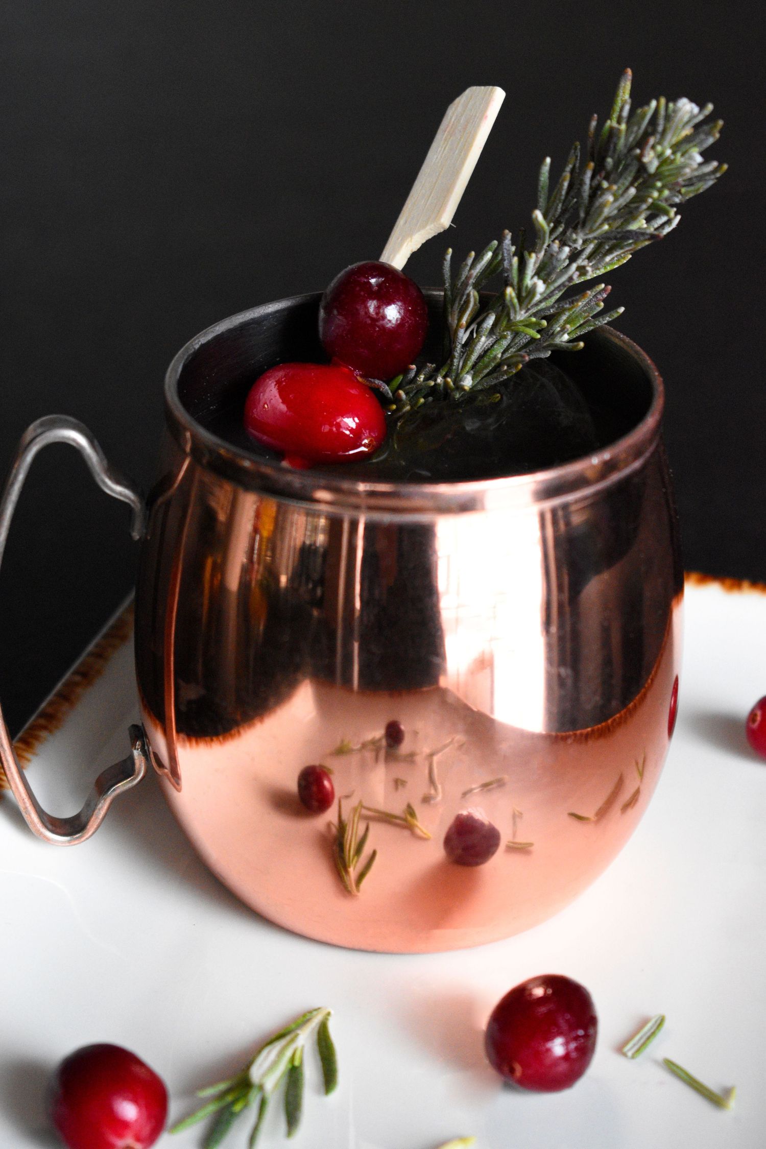 Cranberry Moscow mule in a copper mug garnished with rosemary and fresh cranberries.