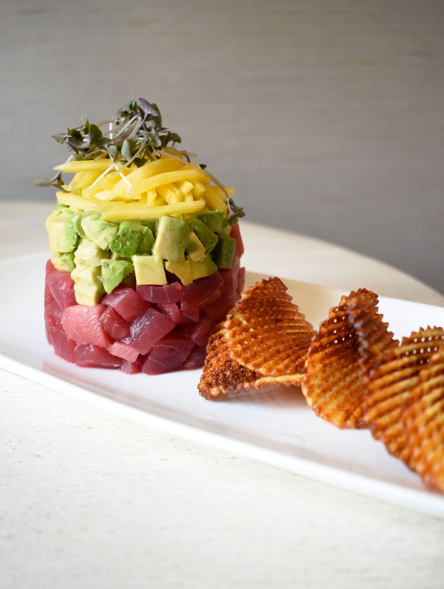 Tuna tartare tower with avocado and mango topped with microgreens served with waffle chips.