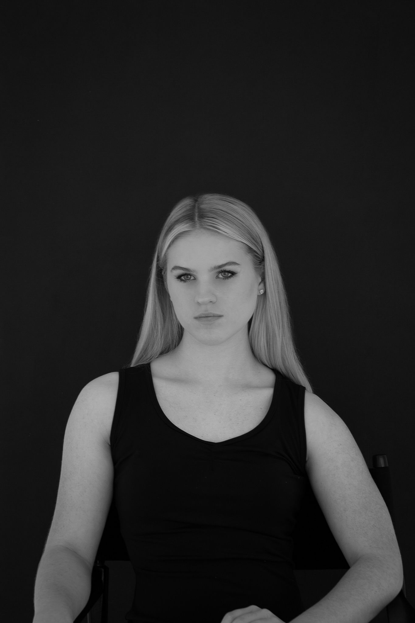 Black and white portrait of a serious blonde woman in black sleeveless top on dark background.