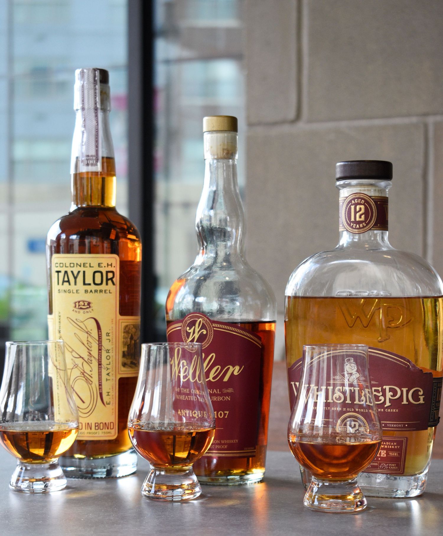 Colonel E.H. Taylor Single Barrel, Weller, and WhistlePig 12 whiskey bottles with Glencairn glasses.