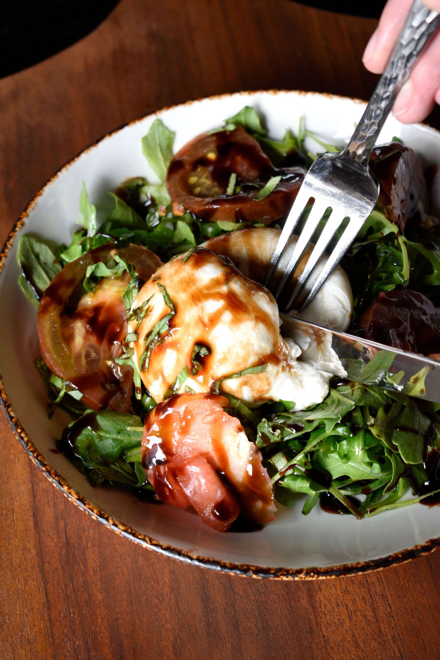 Fresh caprese salad with burrata, heirloom tomatoes, arugula and balsamic glaze served in a rustic bowl.