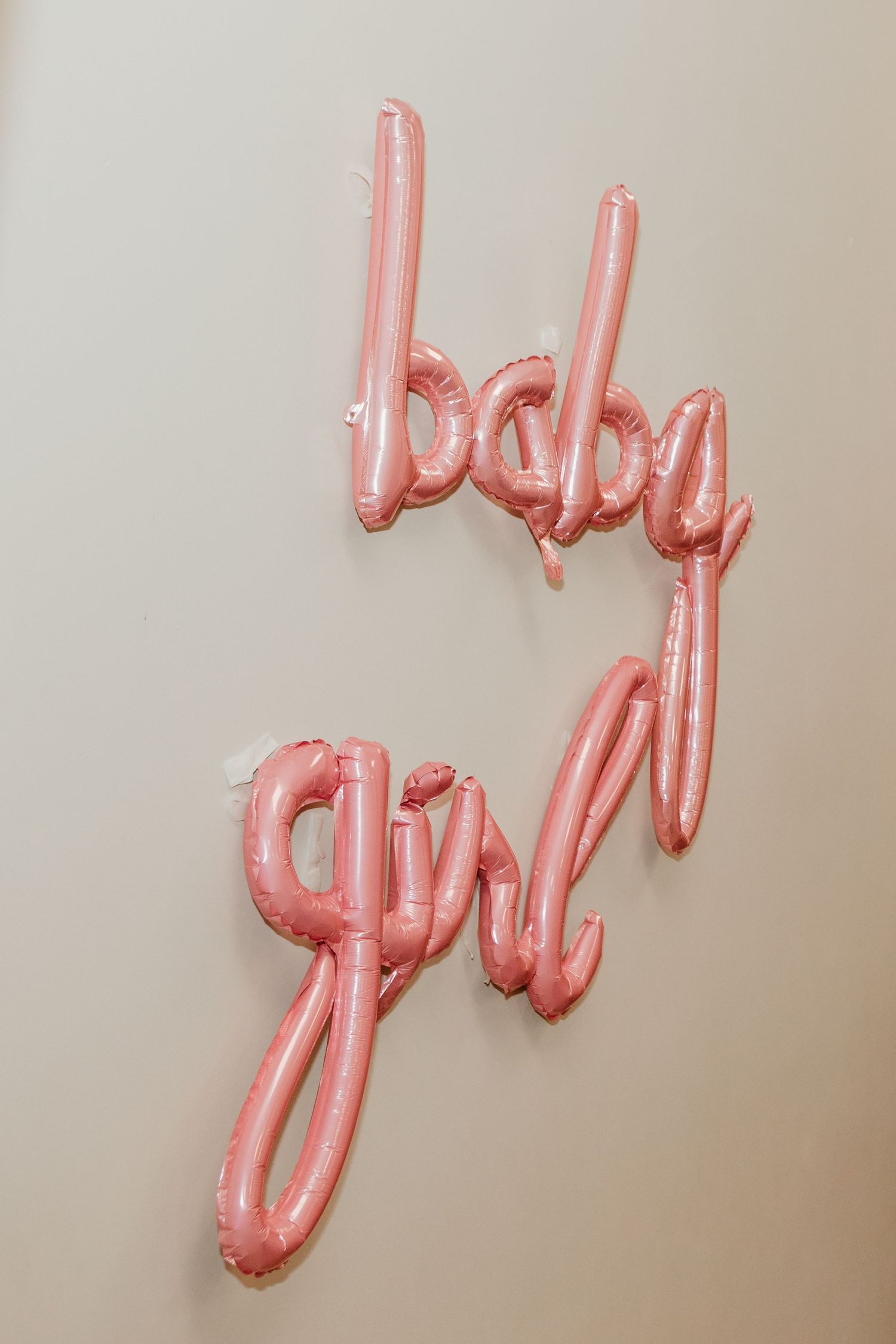 Pink foil balloon letters spelling baby girl mounted on a neutral wall for a baby shower celebration.