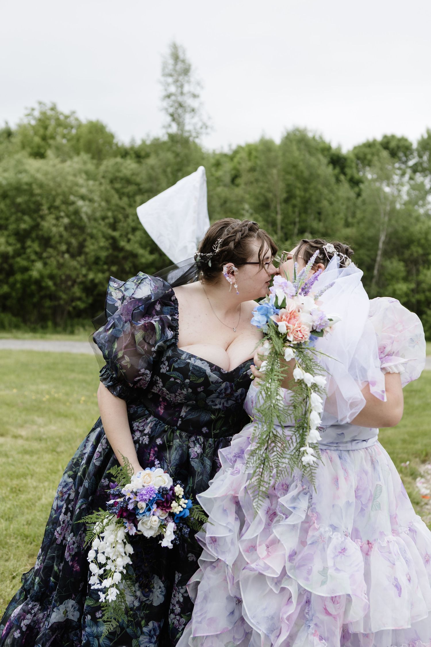 Two brides in floral and lavender gowns share a kiss outdoors, holding bouquets Fredericton New Brunswick Elopement