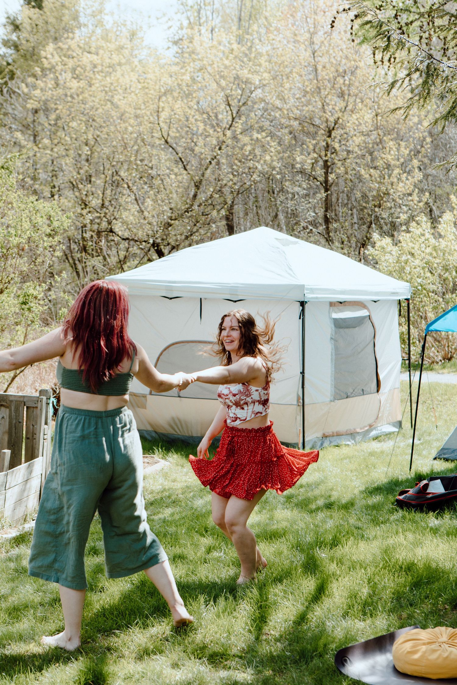 Two women dancing and spinning together outdoors near a white canvas tent on a sunny day.