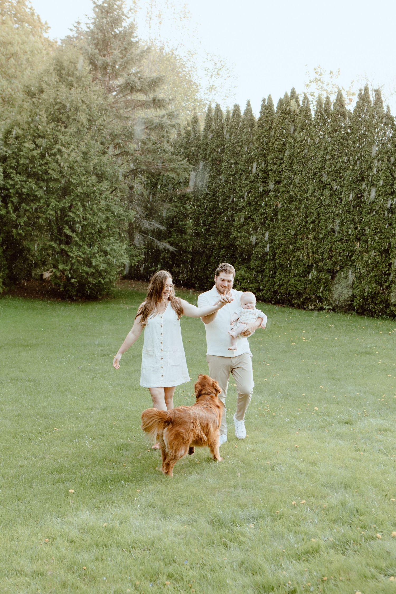 Happy family with baby and golden retriever playing in lush green backyard on a sunny day.