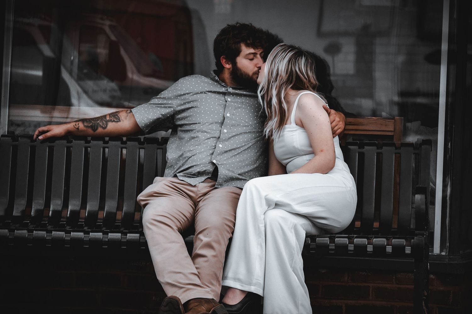 Couple sharing tender moment on wooden bench against industrial brick backdrop.