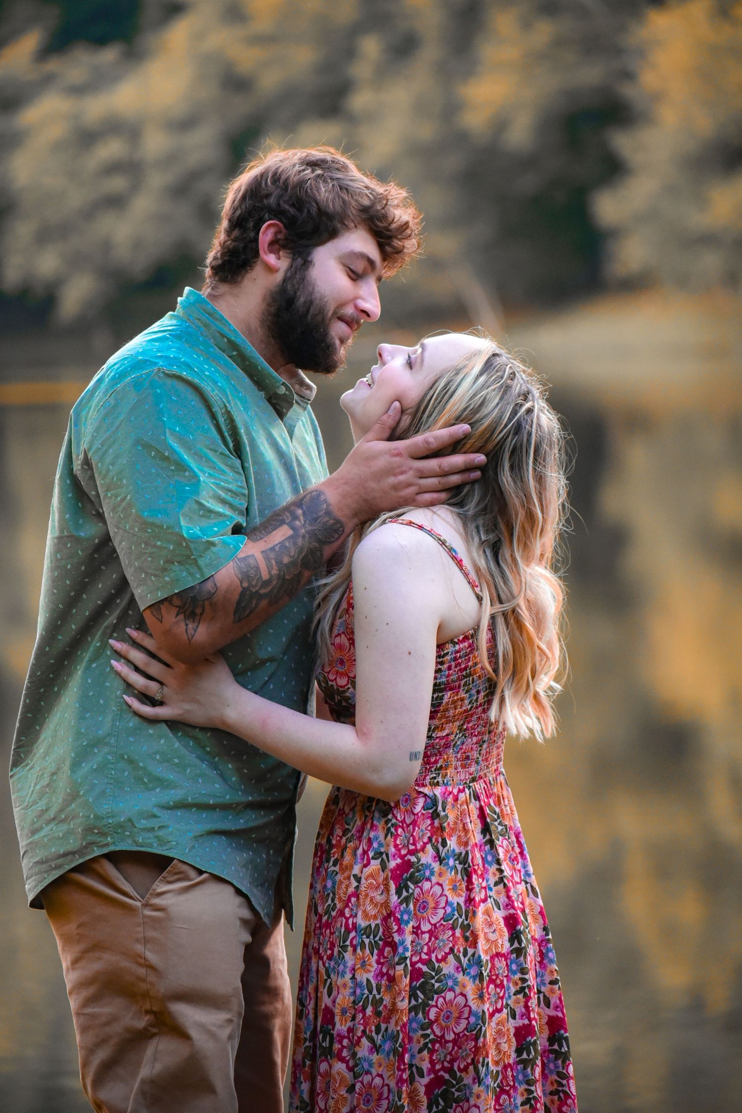 A couple shares a passionate kiss by a lake with autumn colors reflecting in the water.