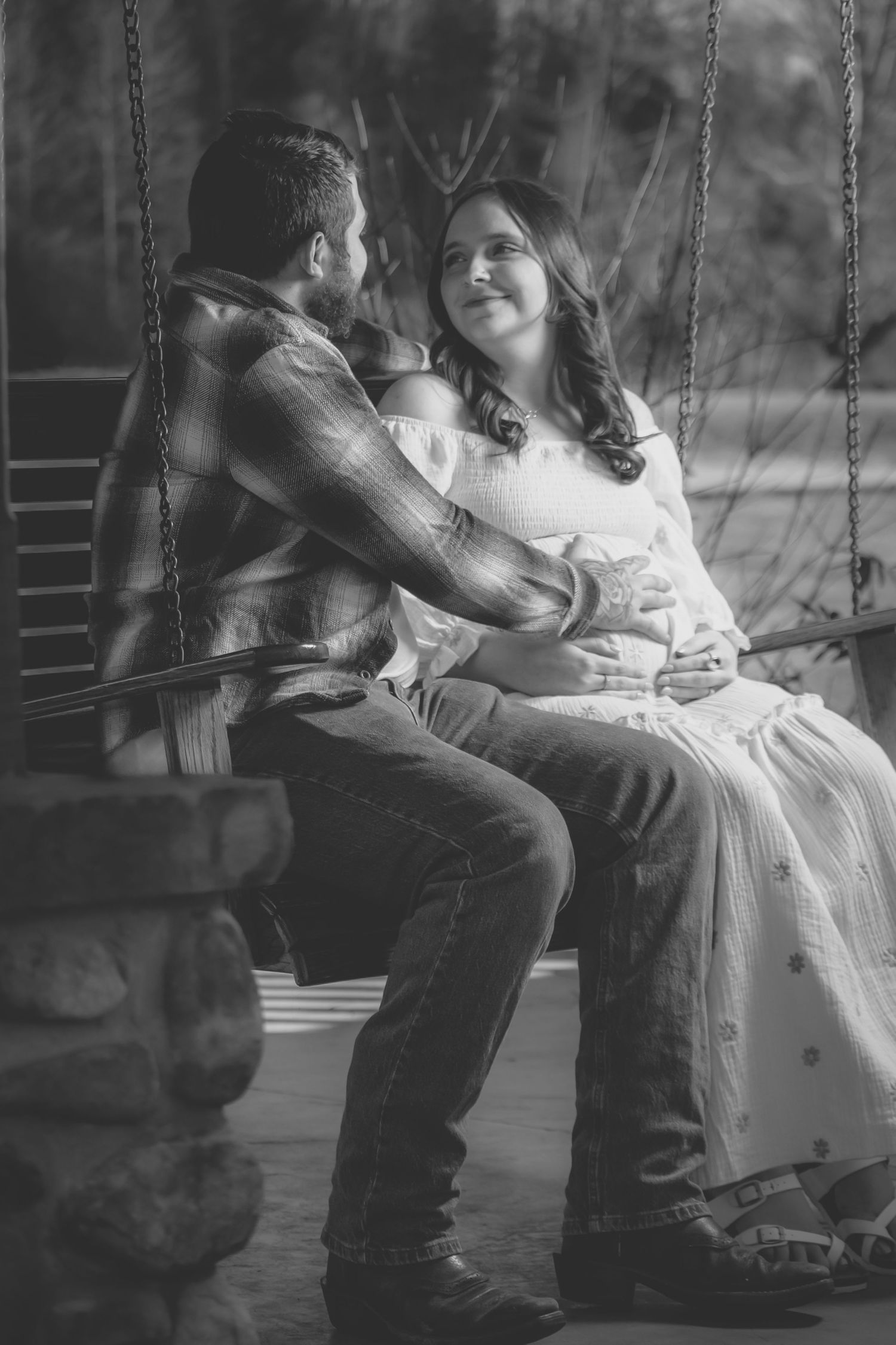 A couple sits together on a porch swing in a romantic black and white photo series.