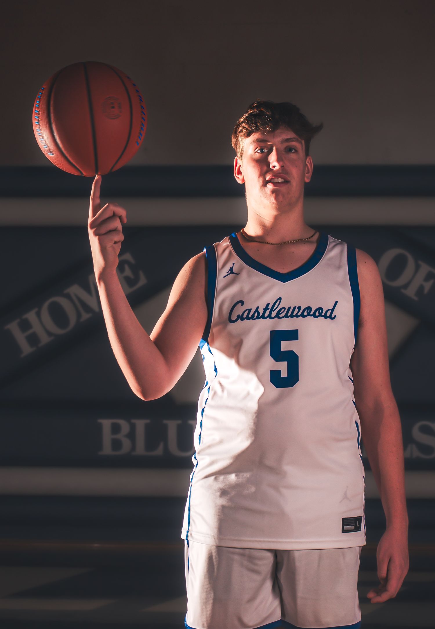 Basketball player in white Castlewood jersey number 5 spins ball on finger during team photo shoot.