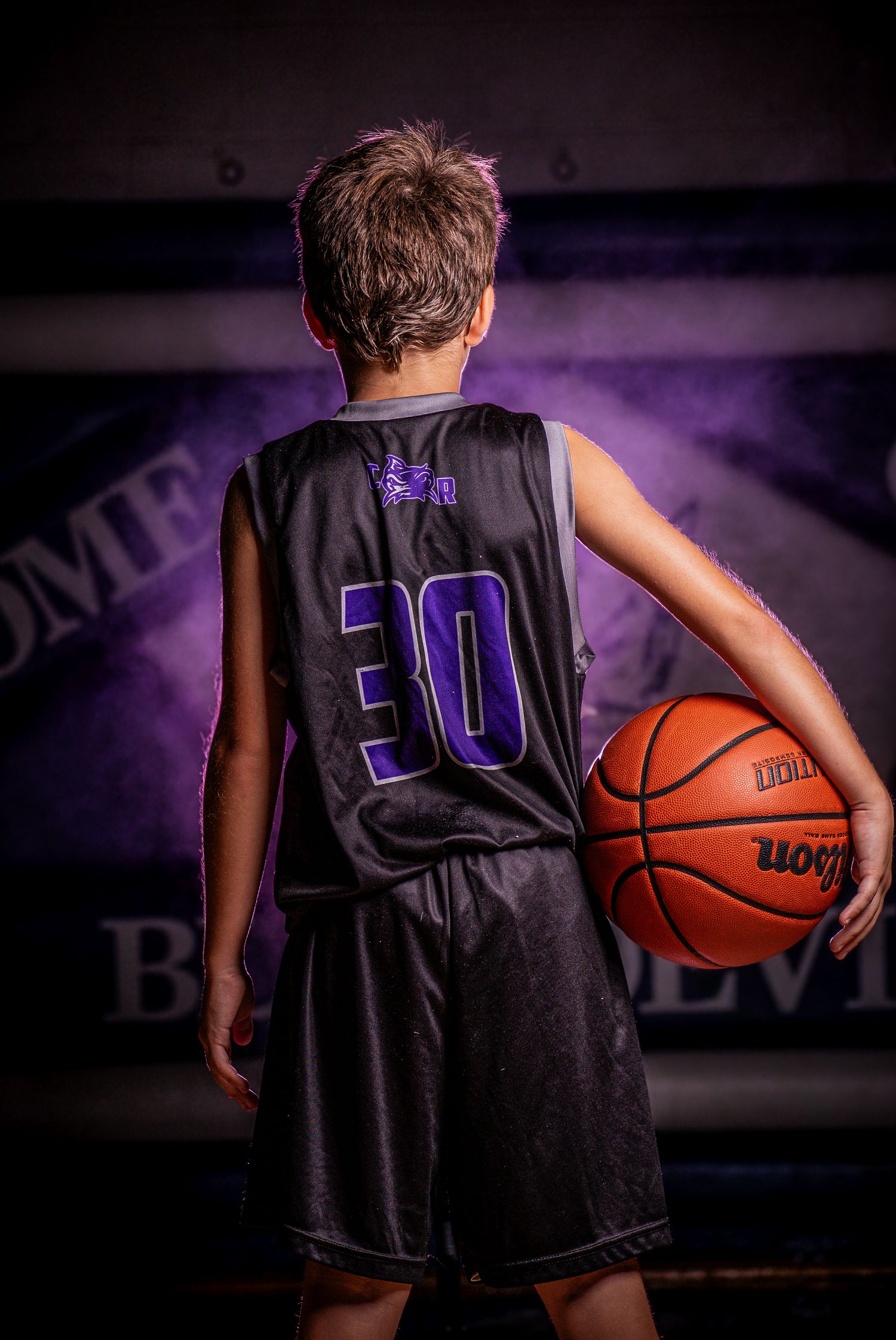 Basketball player wearing jersey number 30 shown from behind holding ball in moody lighting.