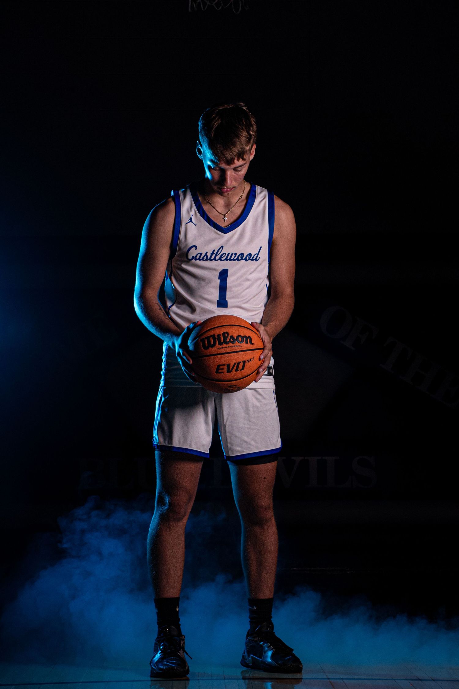 Player in white jersey holds basketball with blue atmospheric lighting and smoke effects.