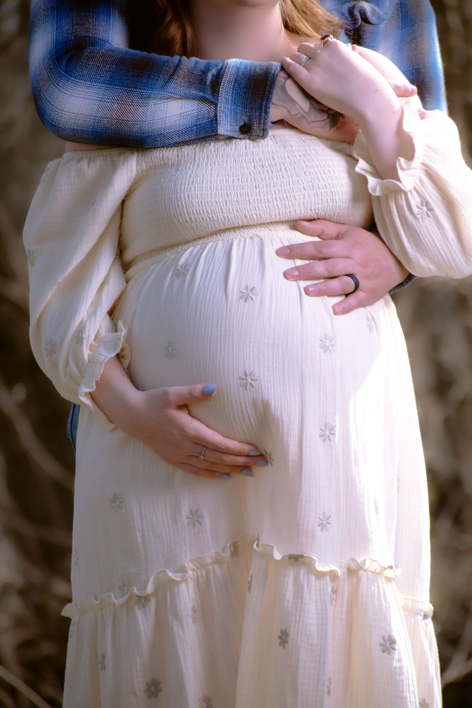 A pregnant belly is gently cradled in a white flowing dress with a denim jacket layered on top.