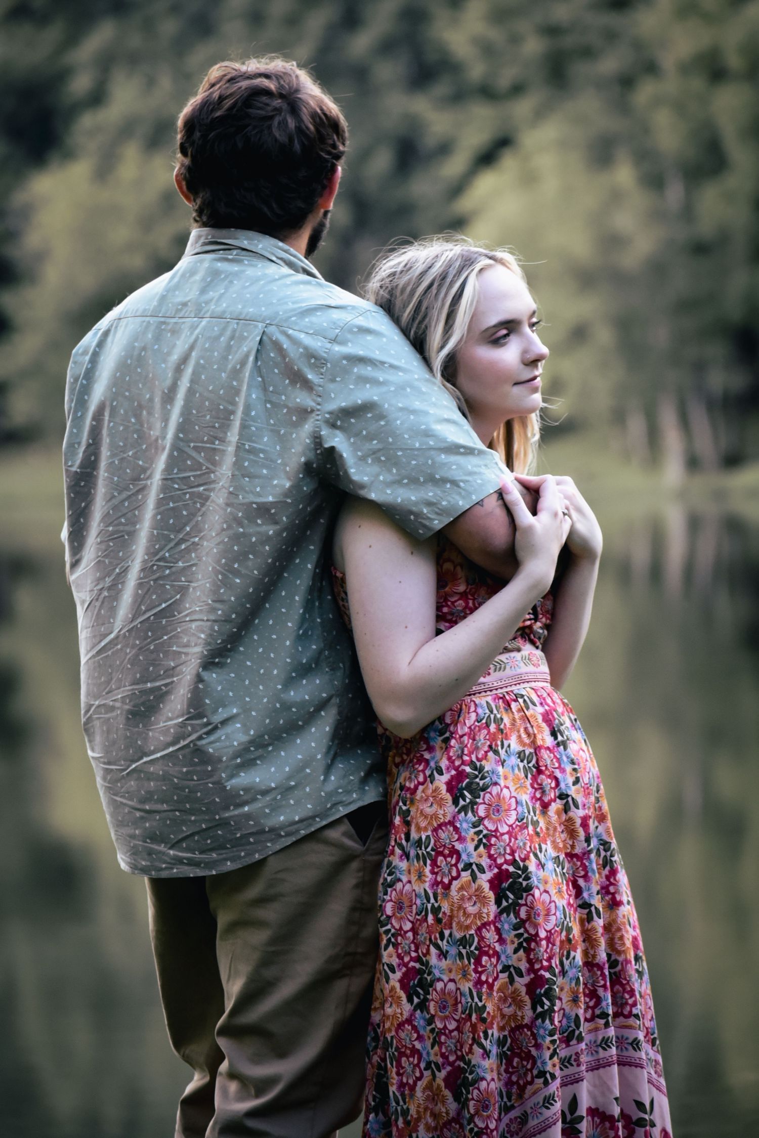 A couple embraces while standing near a peaceful lake during an outdoor photoshoot.