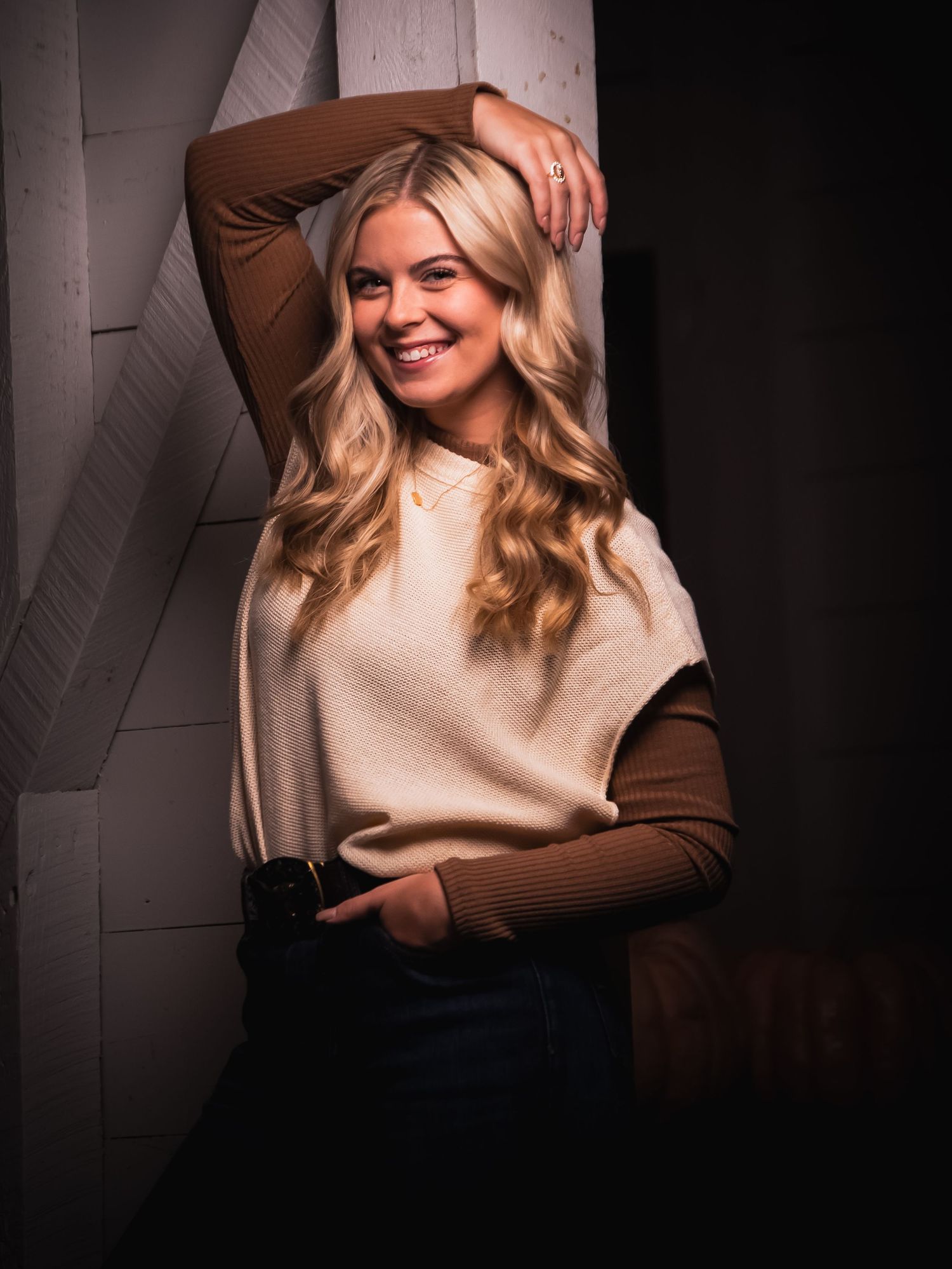 Fashion portrait in beige and brown tones against dark studio backdrop.