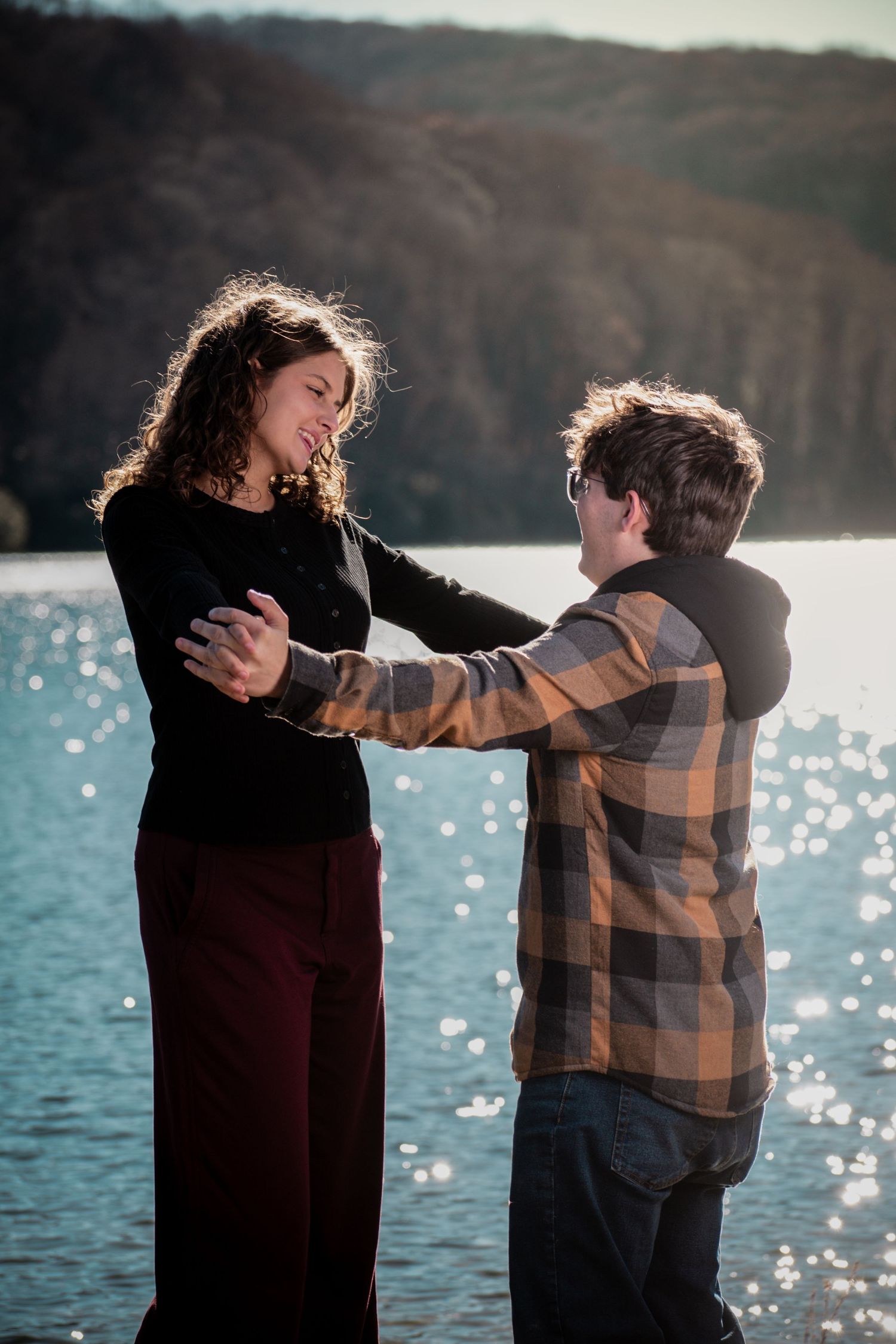 A couple dances playfully by a sparkling lake on a sunny afternoon in a romantic sequence of candid moments.