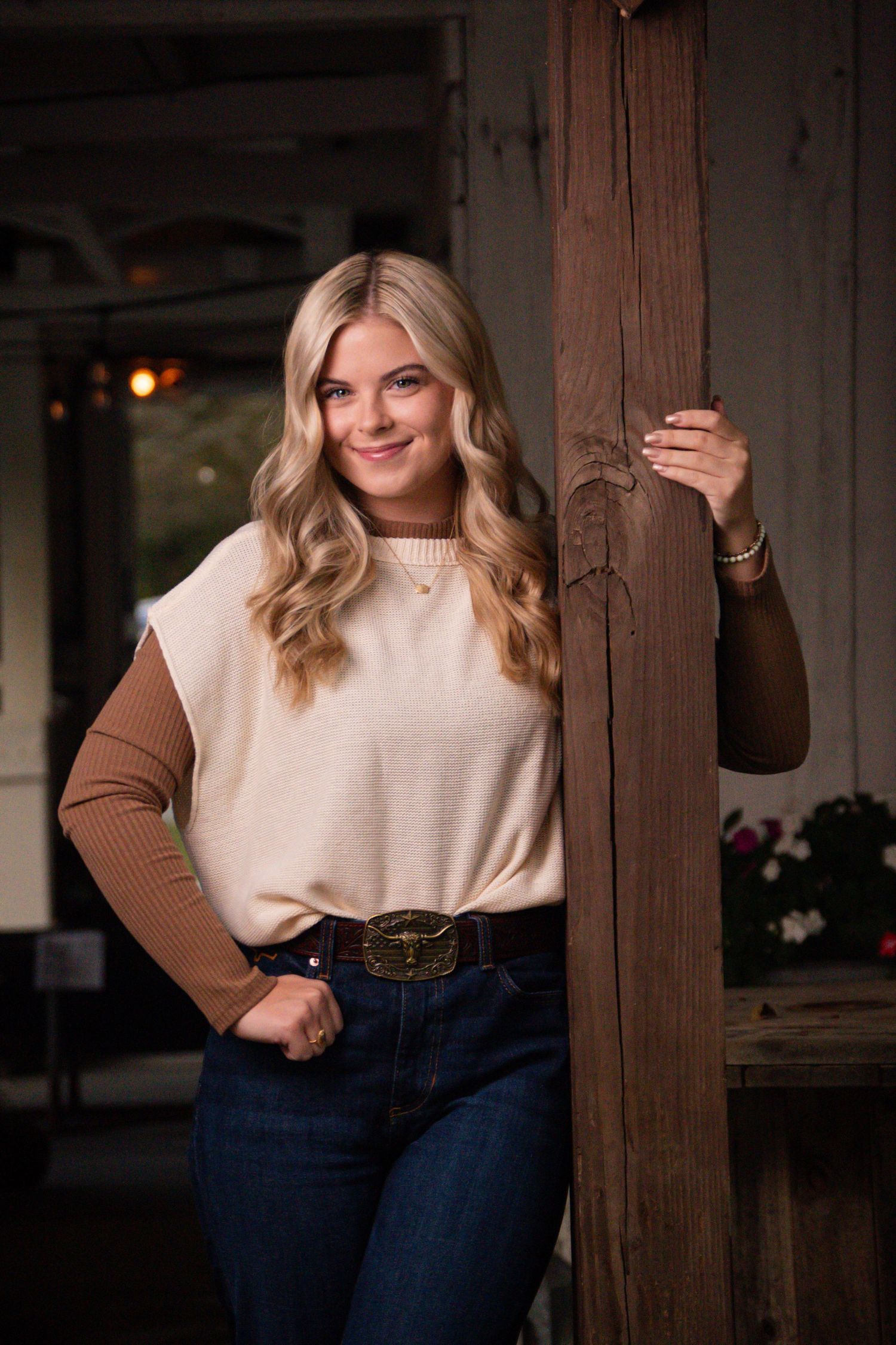 Fashion portrait in cream and brown sweater with dark jeans against rustic wood background.