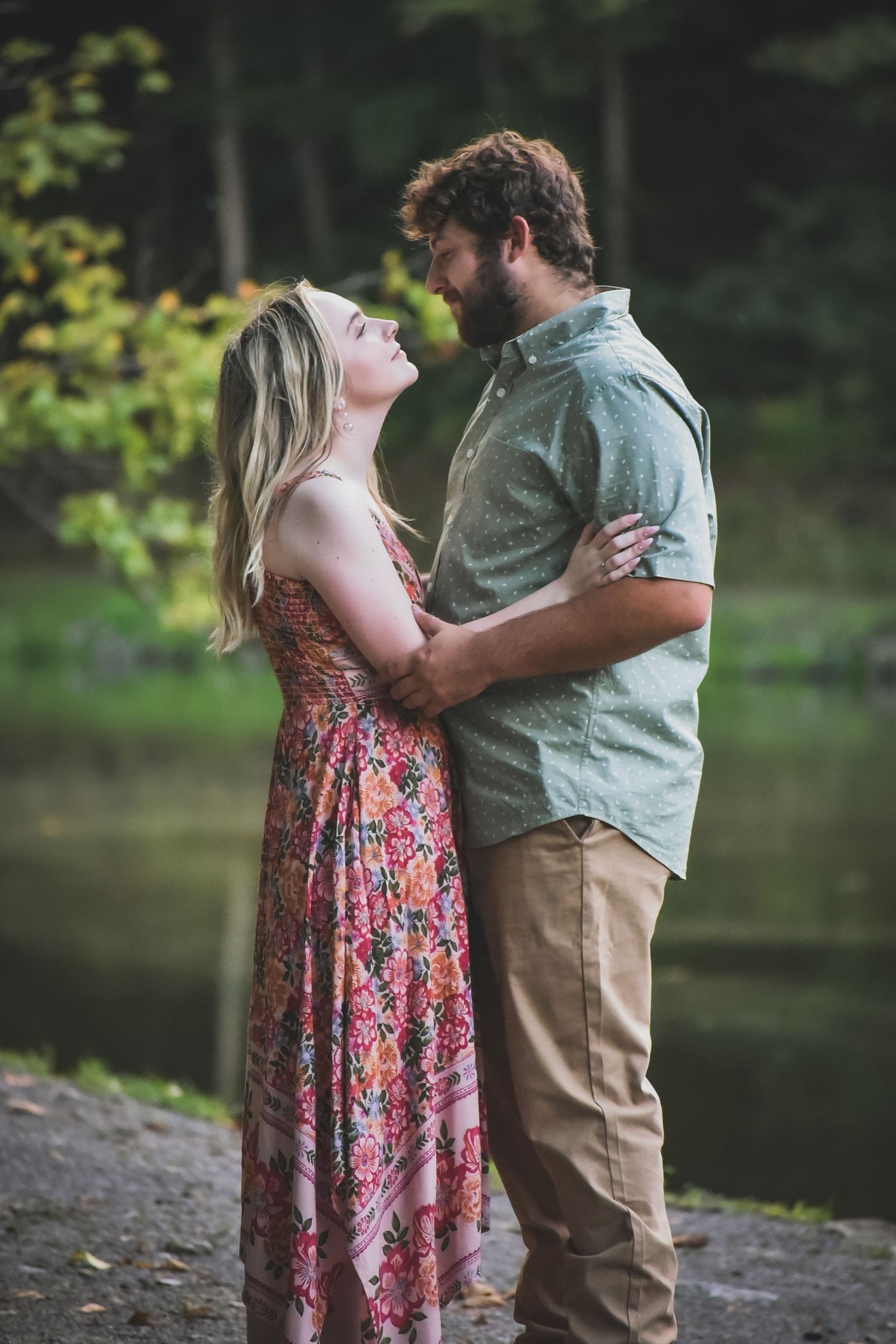 Romantic couple embracing by a lake in casual outdoor attire during sunset.