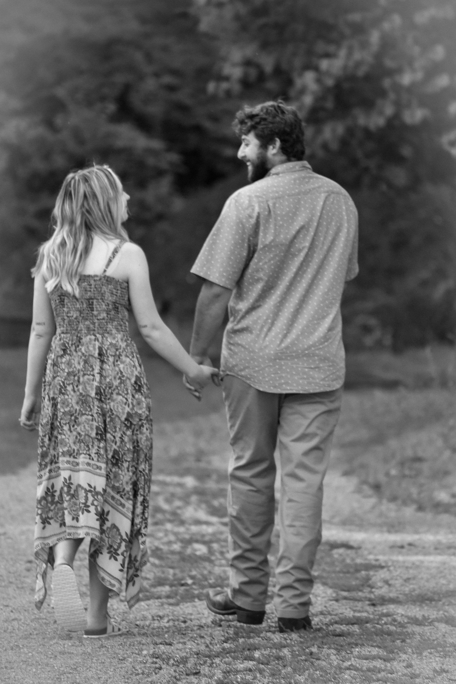 A black and white photo of a couple walking hand in hand by a lake.