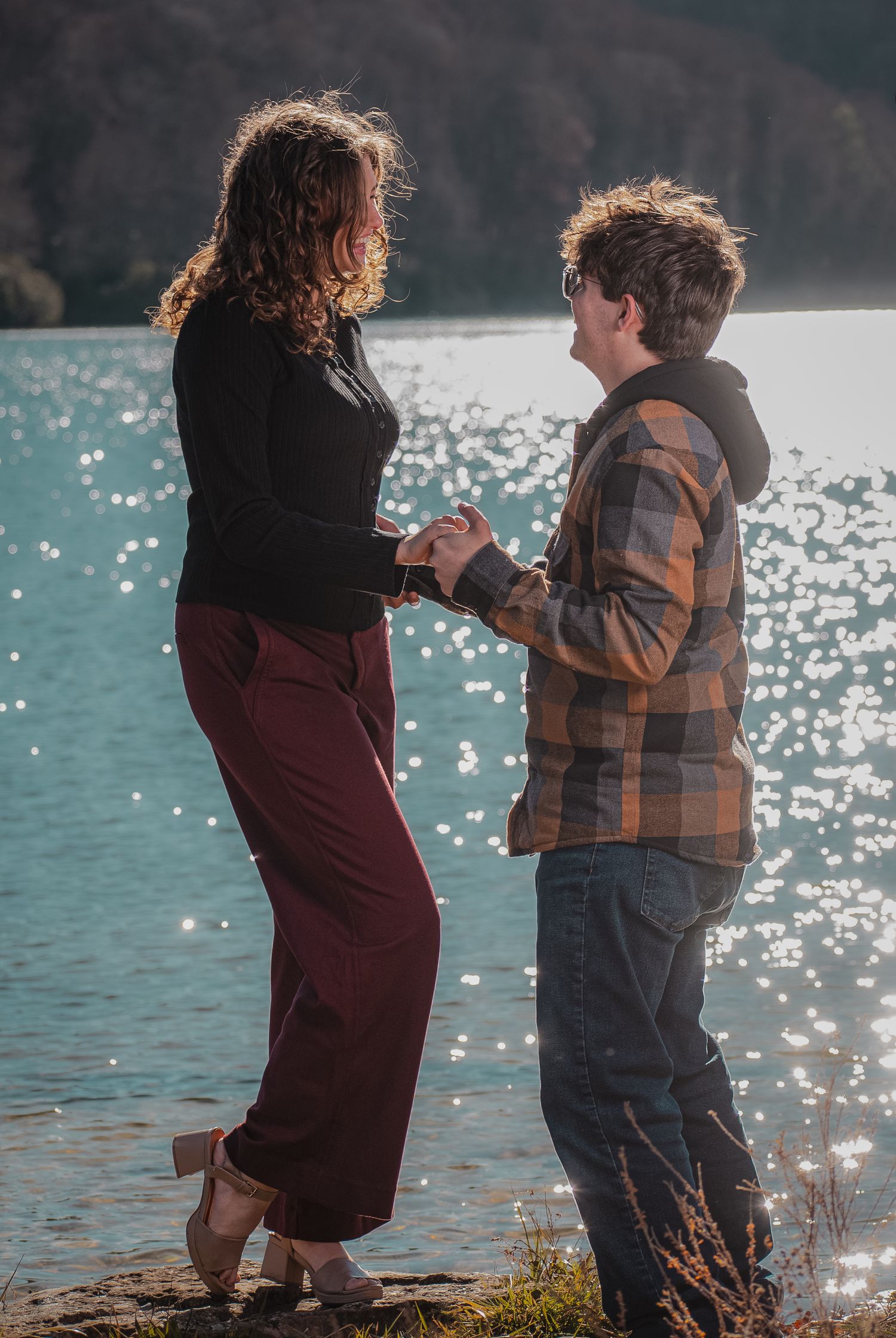A couple dancing and laughing together beside a sparkling lake on a sunny afternoon.