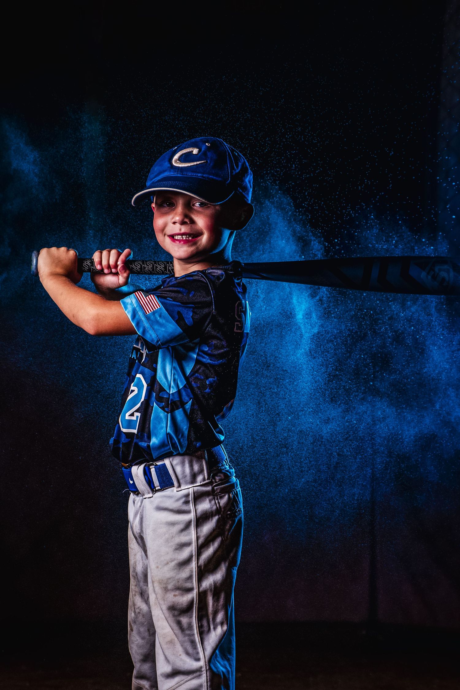 Youth baseball player poses with bat against blue smoke effect background.