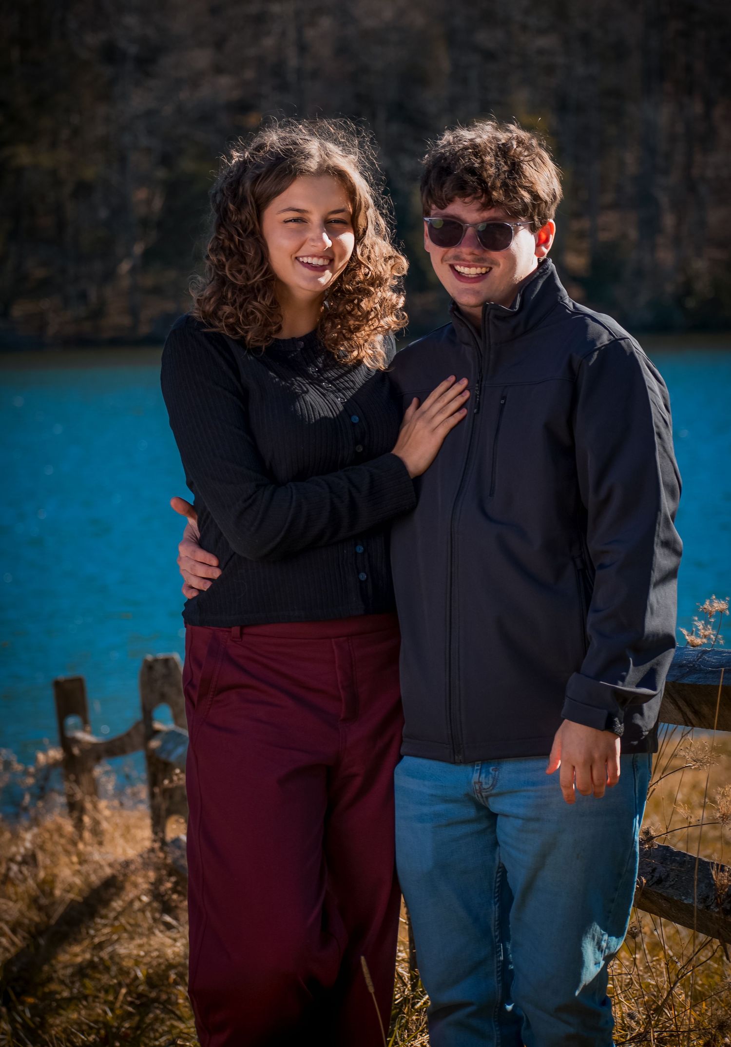 A couple shares a joyful moment together by a stunning turquoise lake against rocky cliffs on a sunny day.
