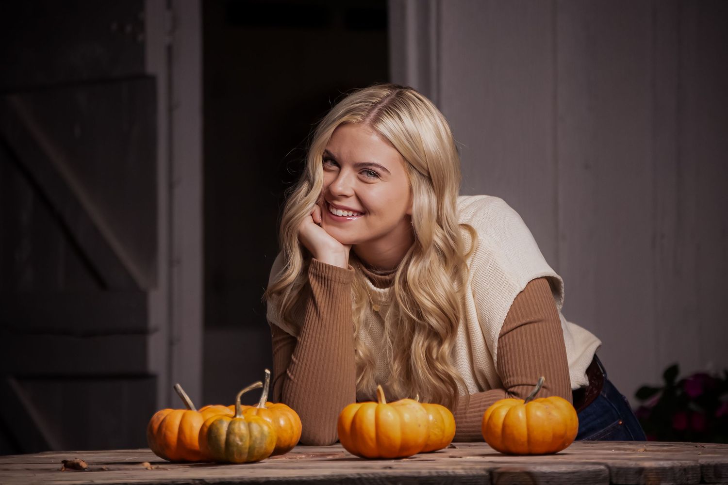 Autumn portrait with orange pumpkins and a cream sweater in moody lighting.