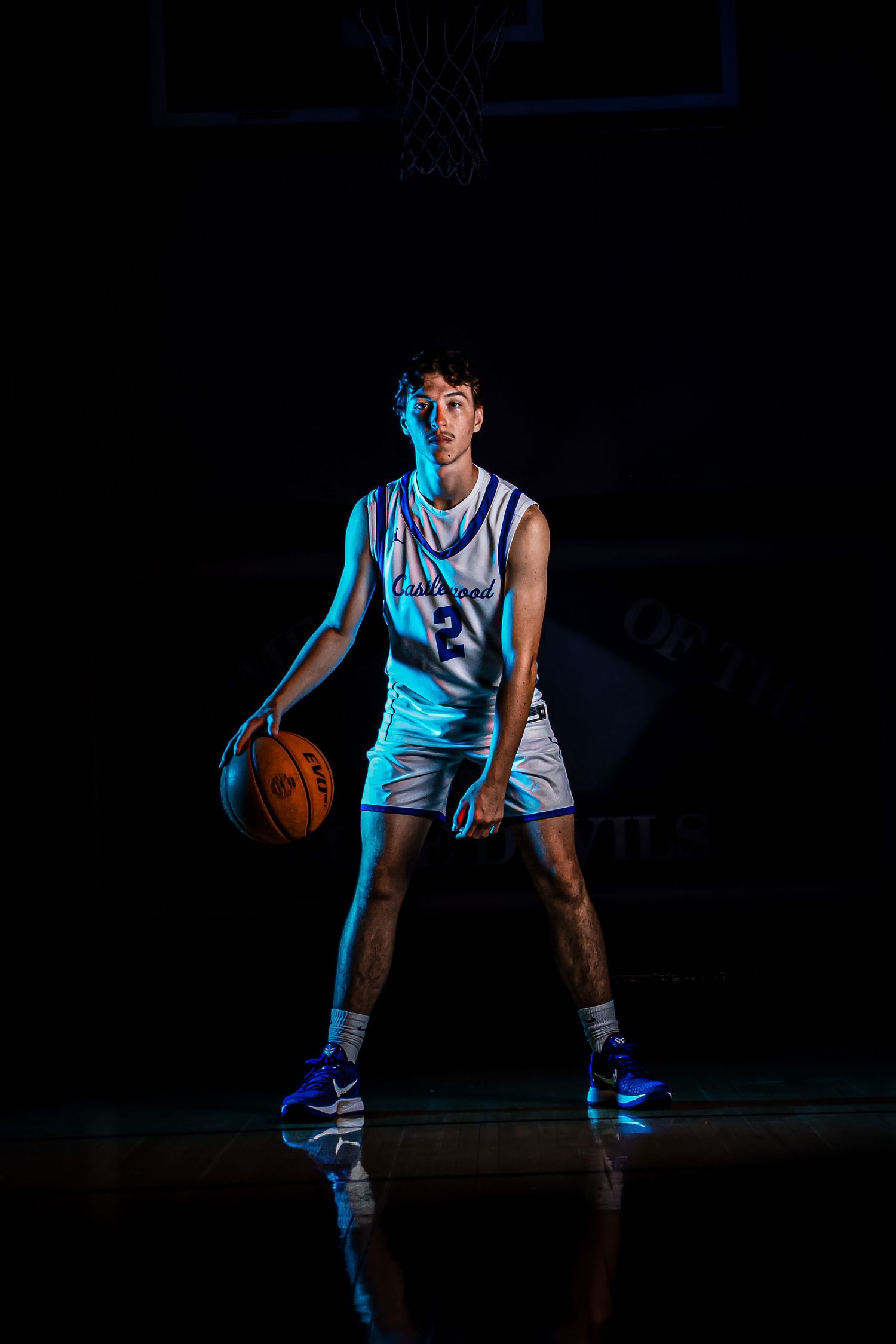 Basketball player demonstrates dribbling stance under dramatic blue lighting.