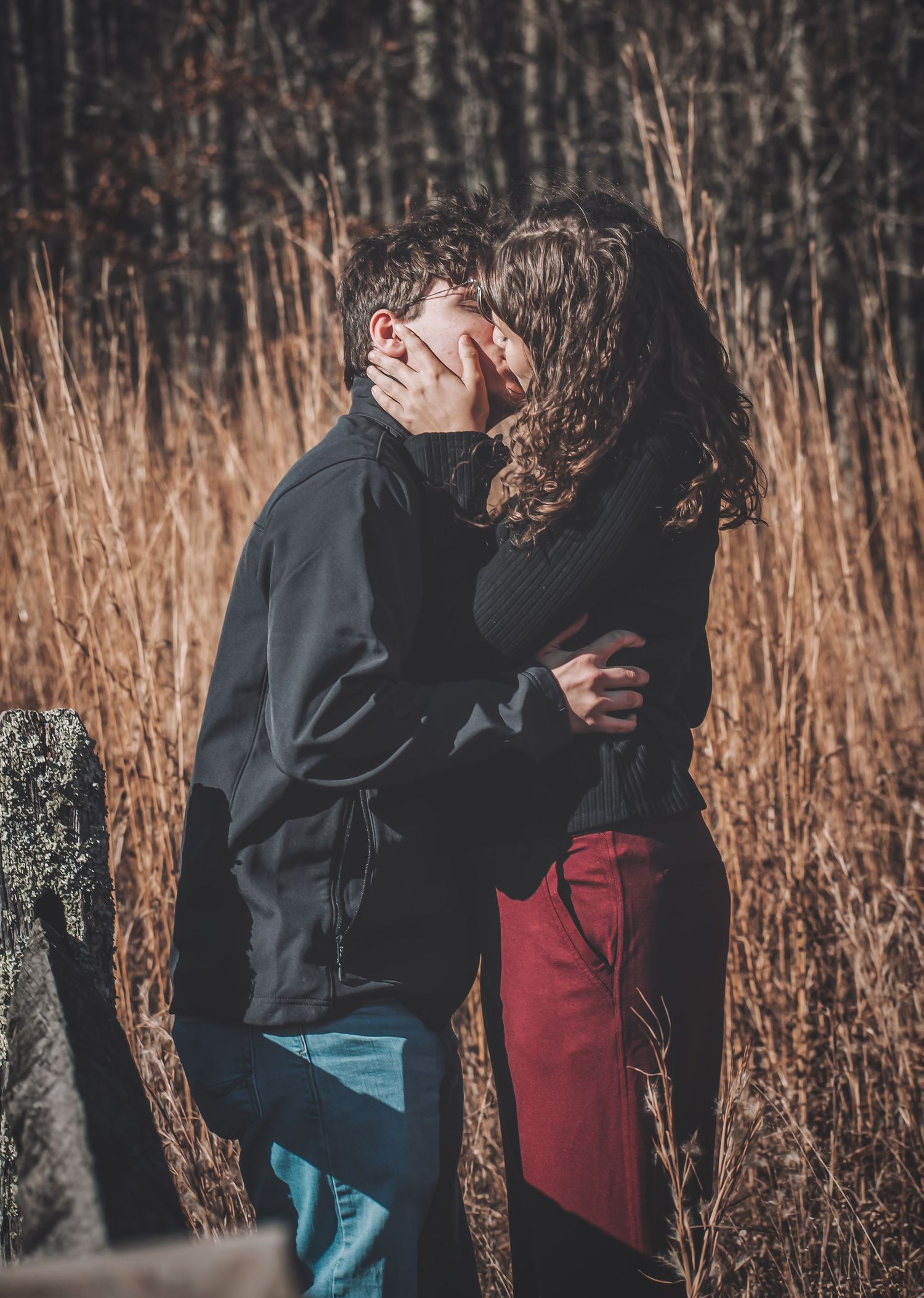 A couple embraces in tall brown grass at sunset creating a romantic silhouette against the natural backdrop.