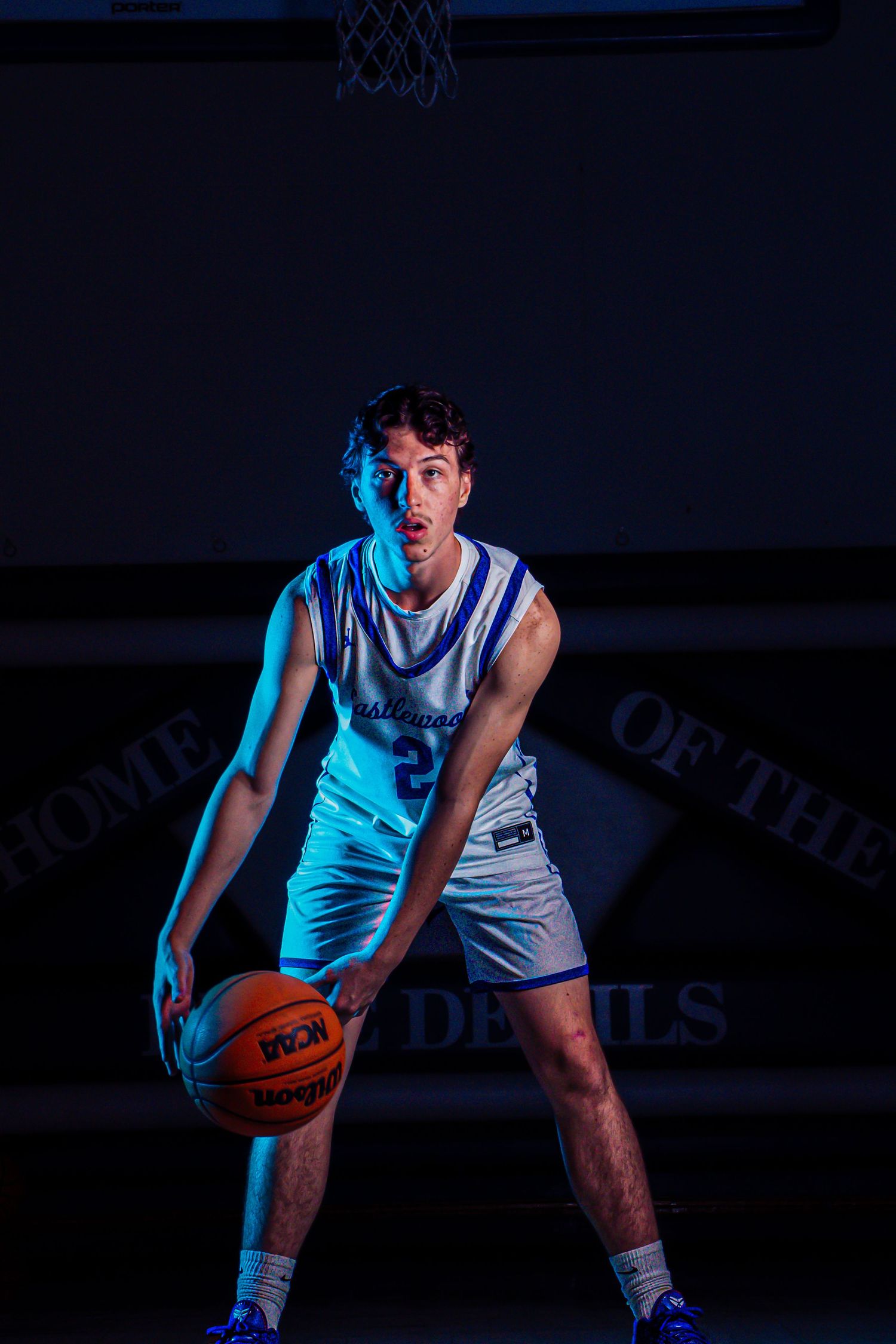 Player dribbles basketball in dramatic blue-lit sports photography setup.