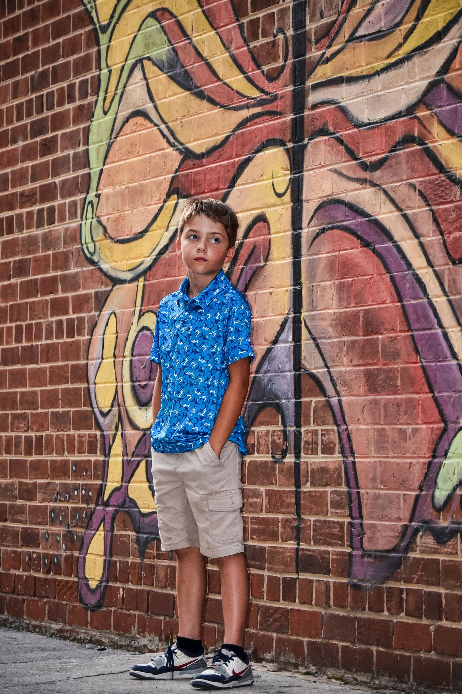 Person in blue patterned shirt poses against colorful graffiti brick wall.