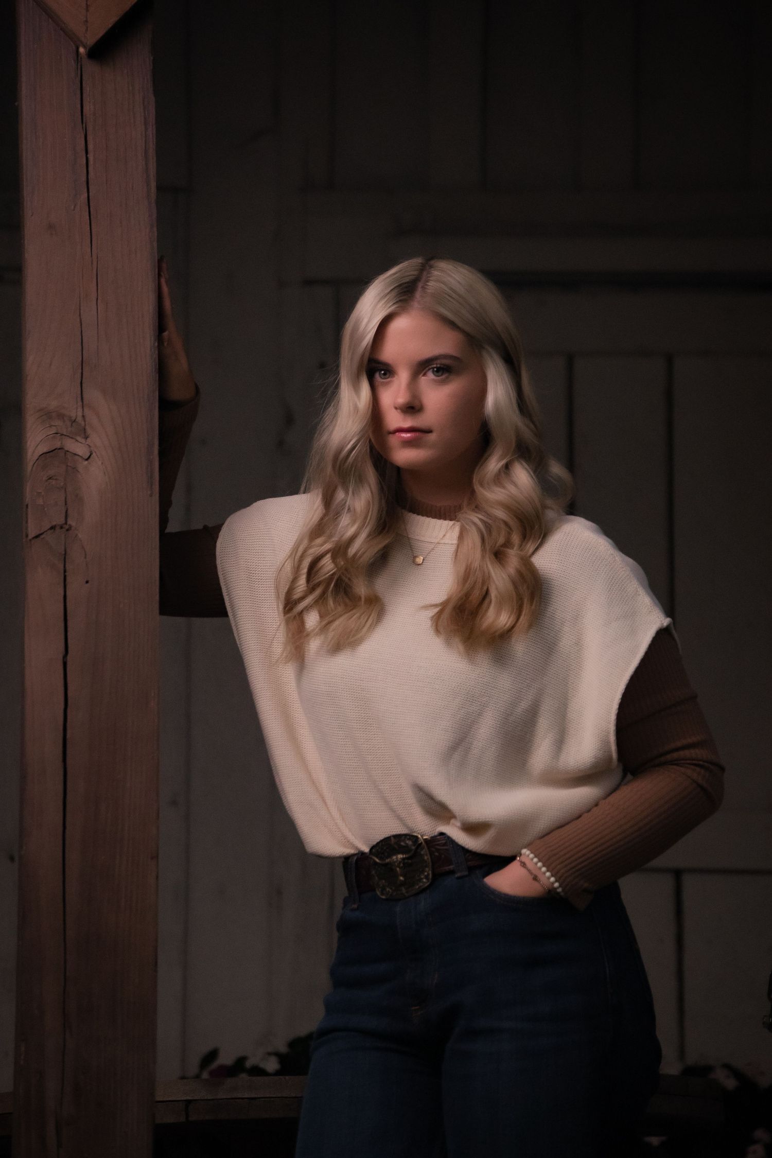 Stylish casual outfit featuring a cream top with brown sleeves and high-waisted jeans in a dark indoor setting.