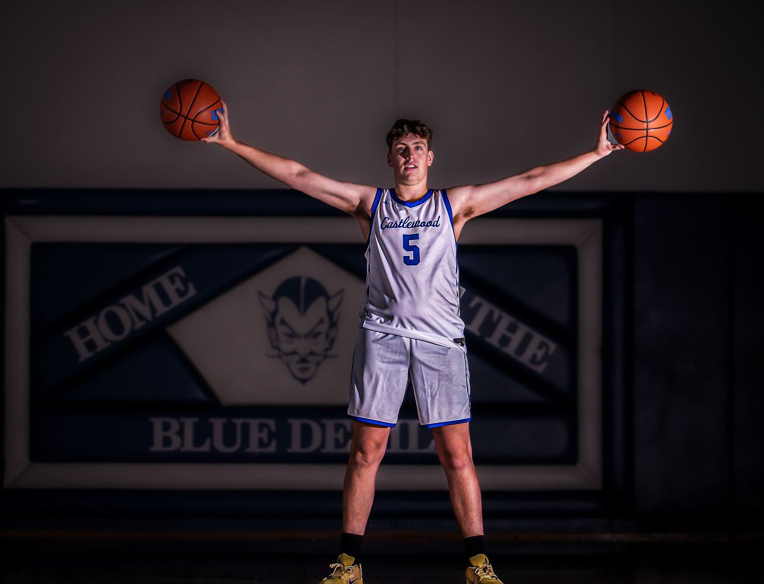 Basketball player in white jersey poses with basketballs in dramatic lighting.