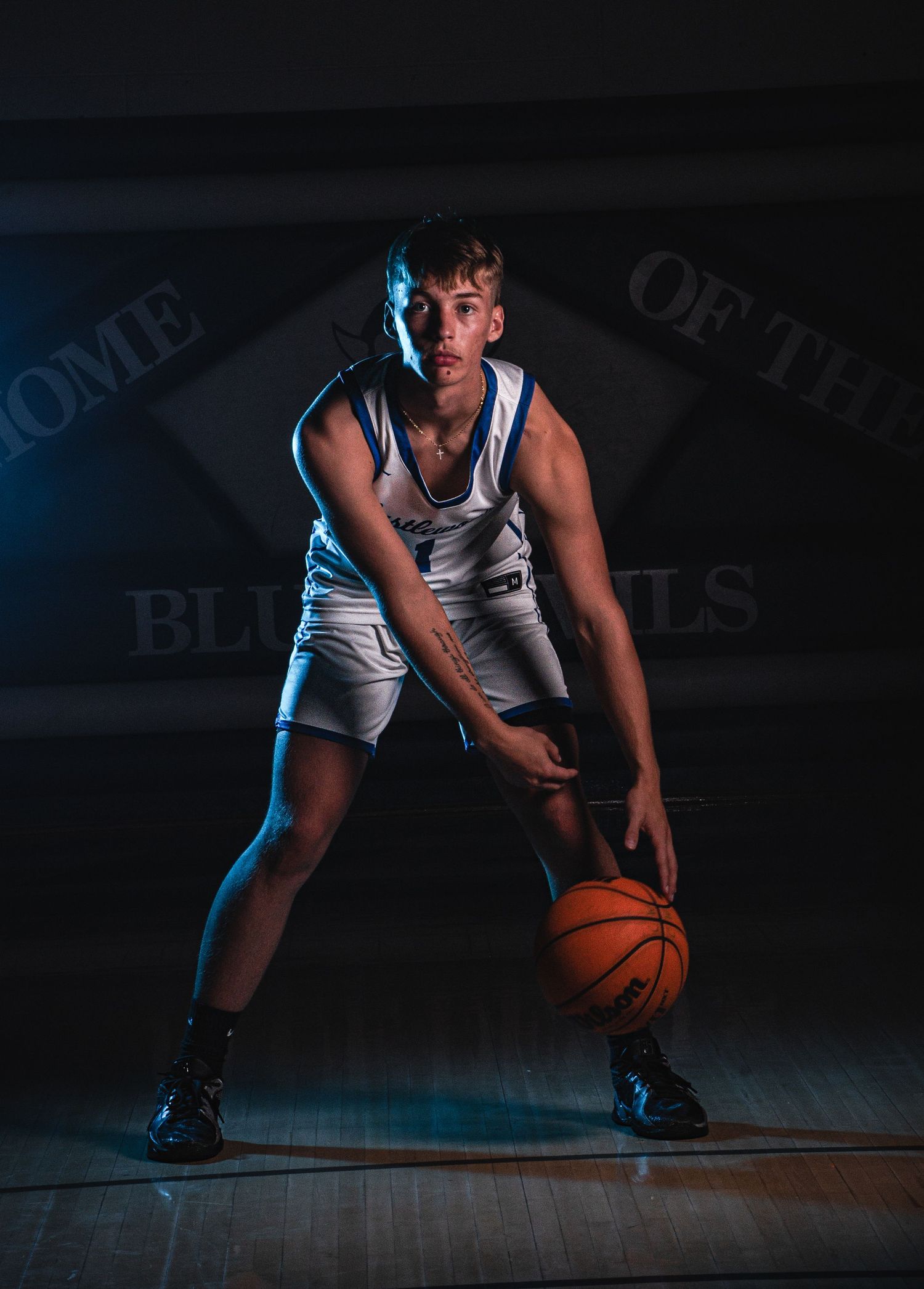 Basketball player crouches low while dribbling ball on court in dramatic lighting.