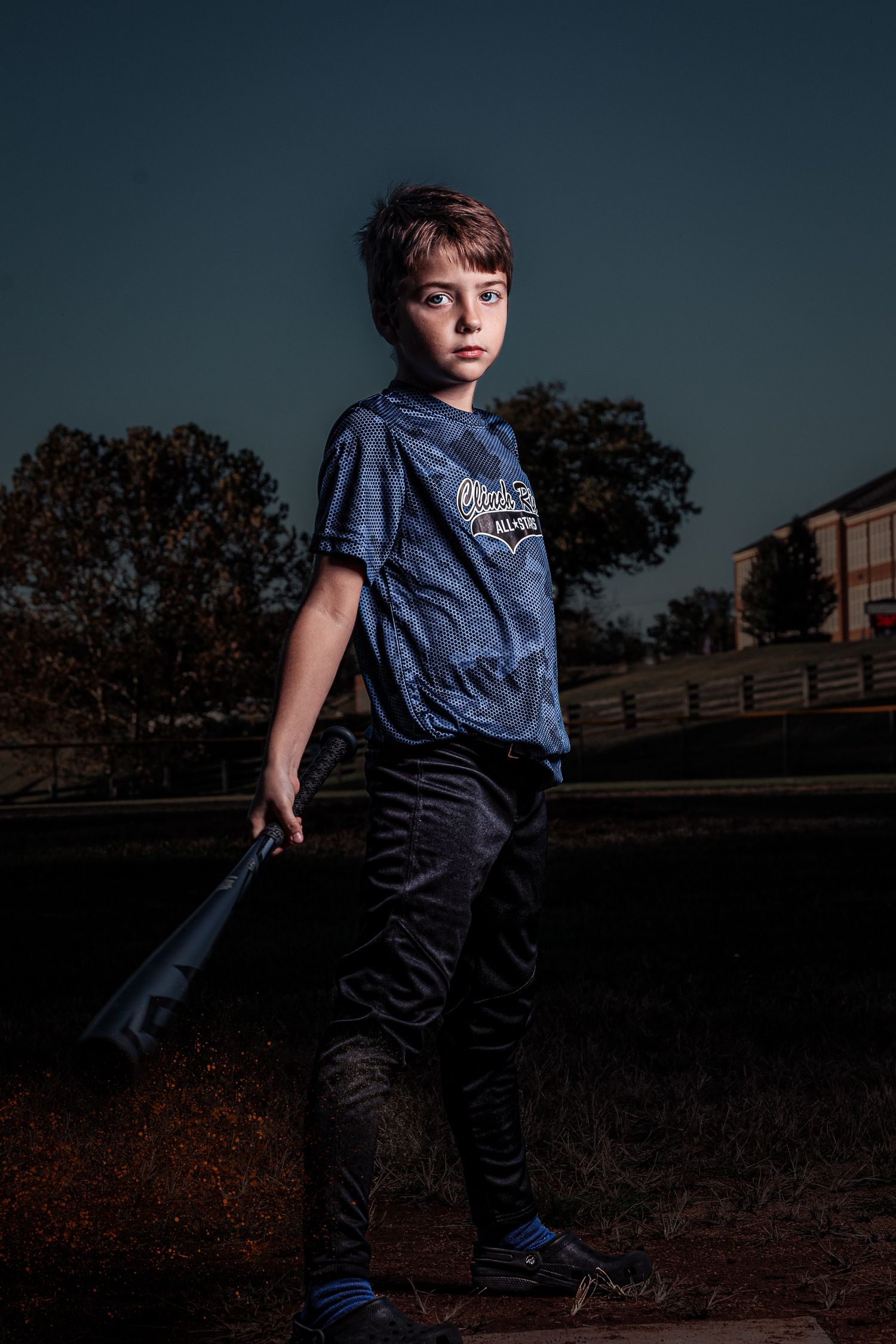 Baseball player poses in dramatic dusk lighting on hillside.
