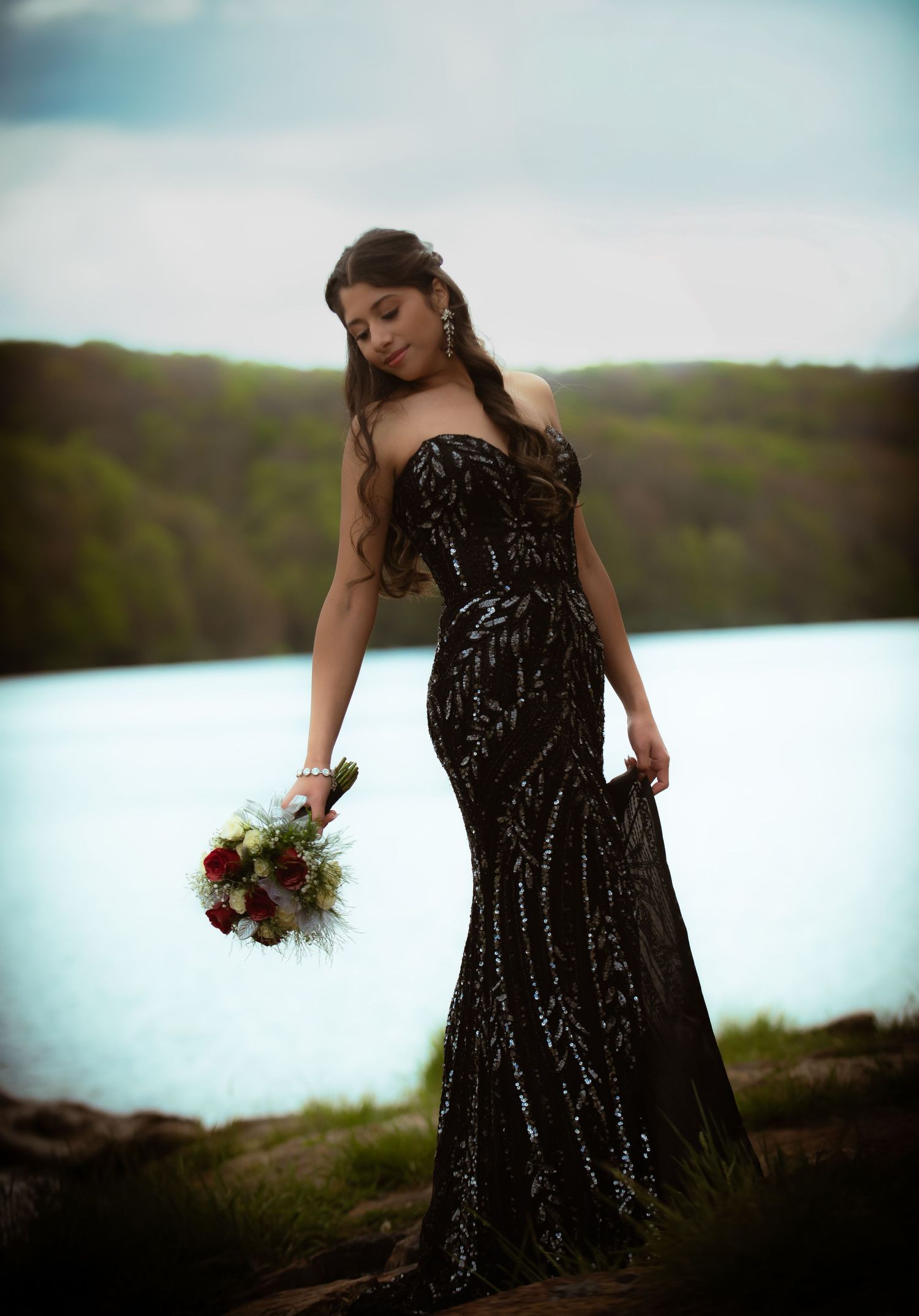 Woman in black sequin strapless mermaid gown holding bouquet by lake.