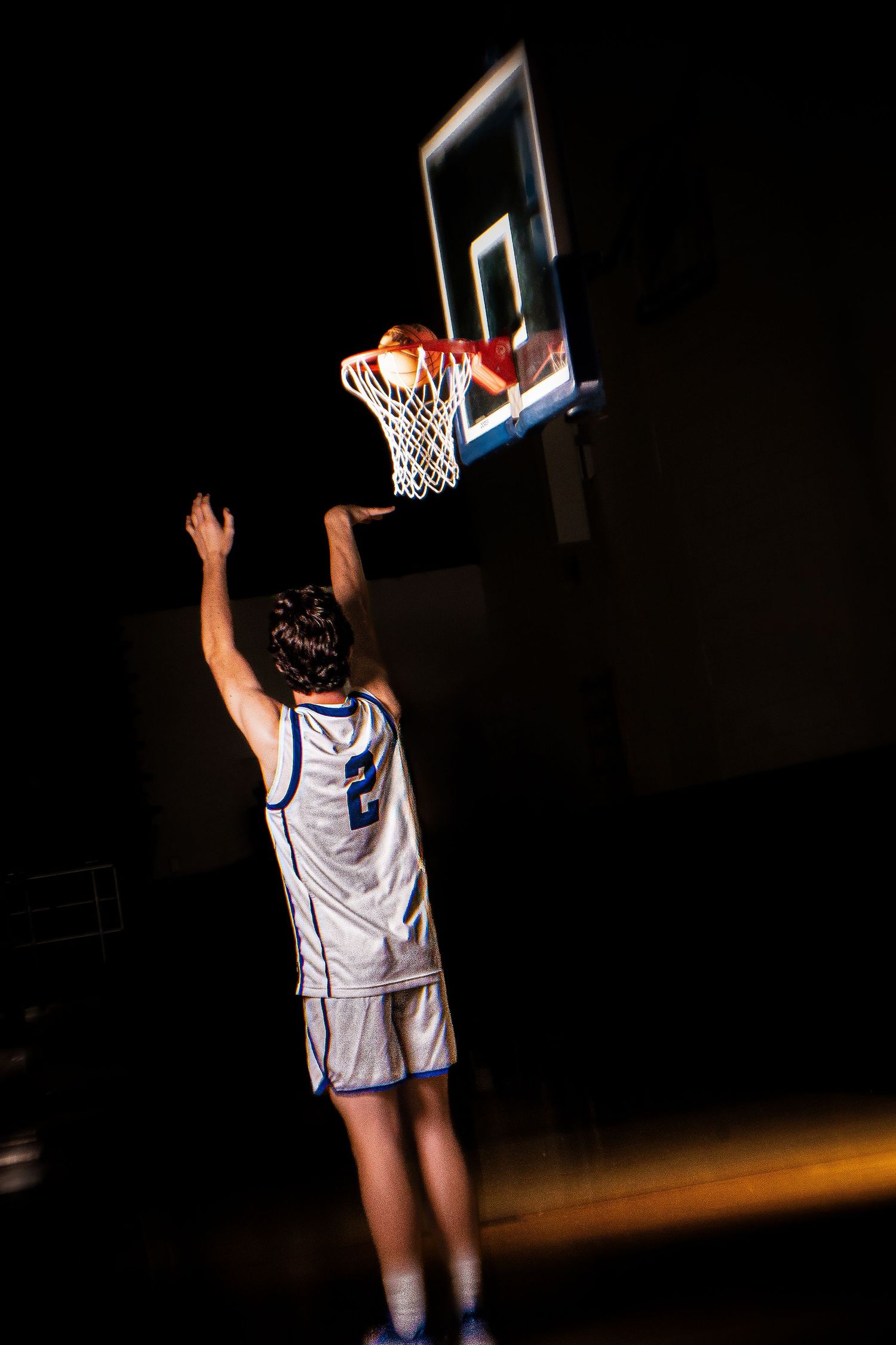 Basketball player reaches up for layup at illuminated hoop.
