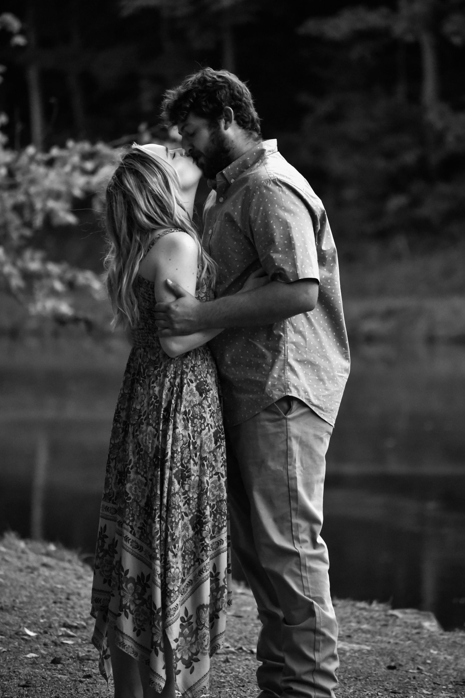 A black and white photo captures an intimate moment between a couple by a lake.