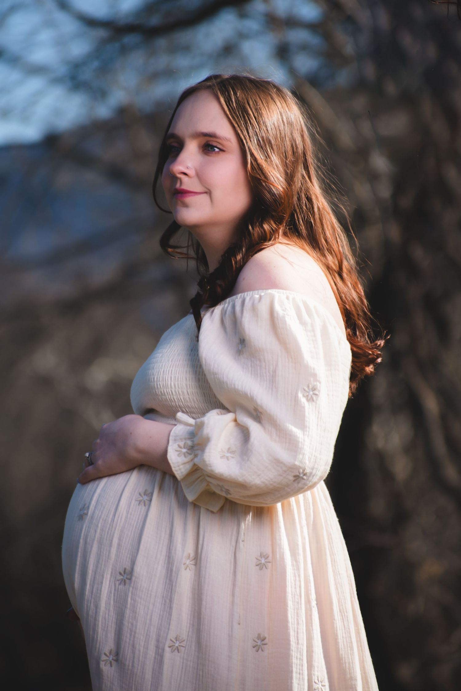 A woman in a cream-colored sweater dress poses outdoors against a blurred natural background.