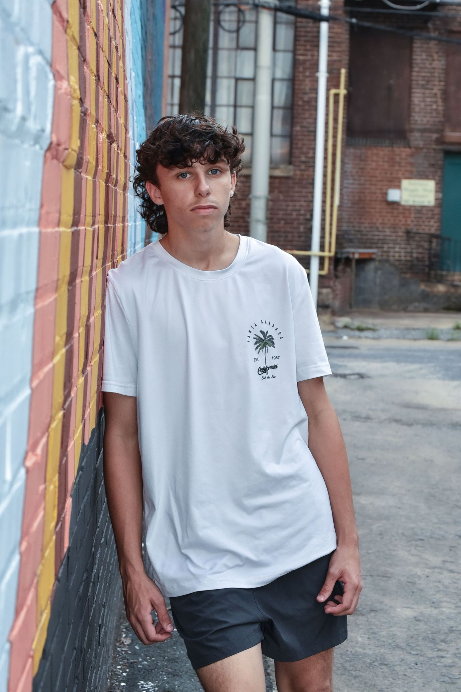 Urban fashion shoot featuring white t-shirt against colorful painted brick wall.