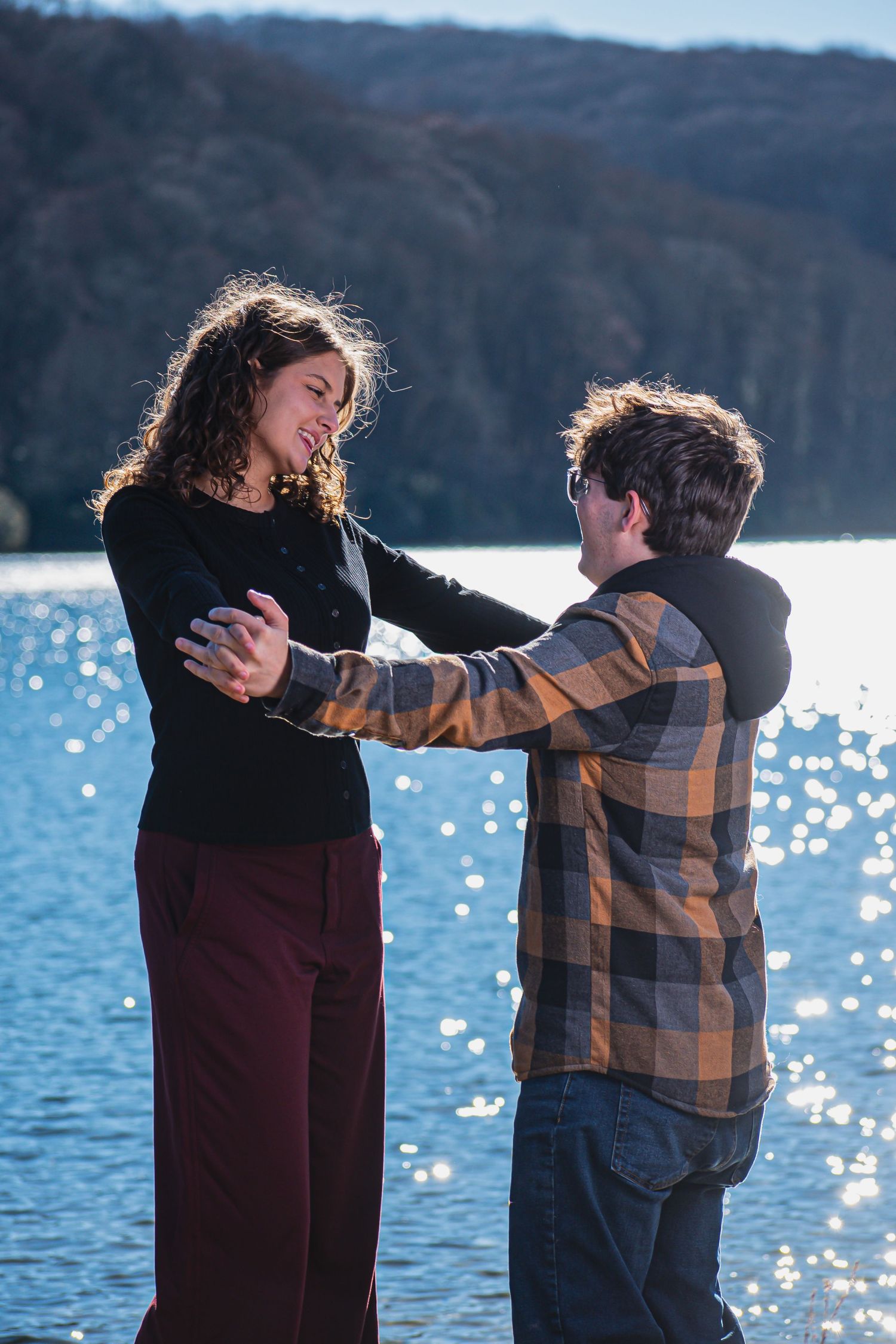 Two people dance together by a sparkling lake on a sunny winter day, their silhouettes creating a romantic moment.