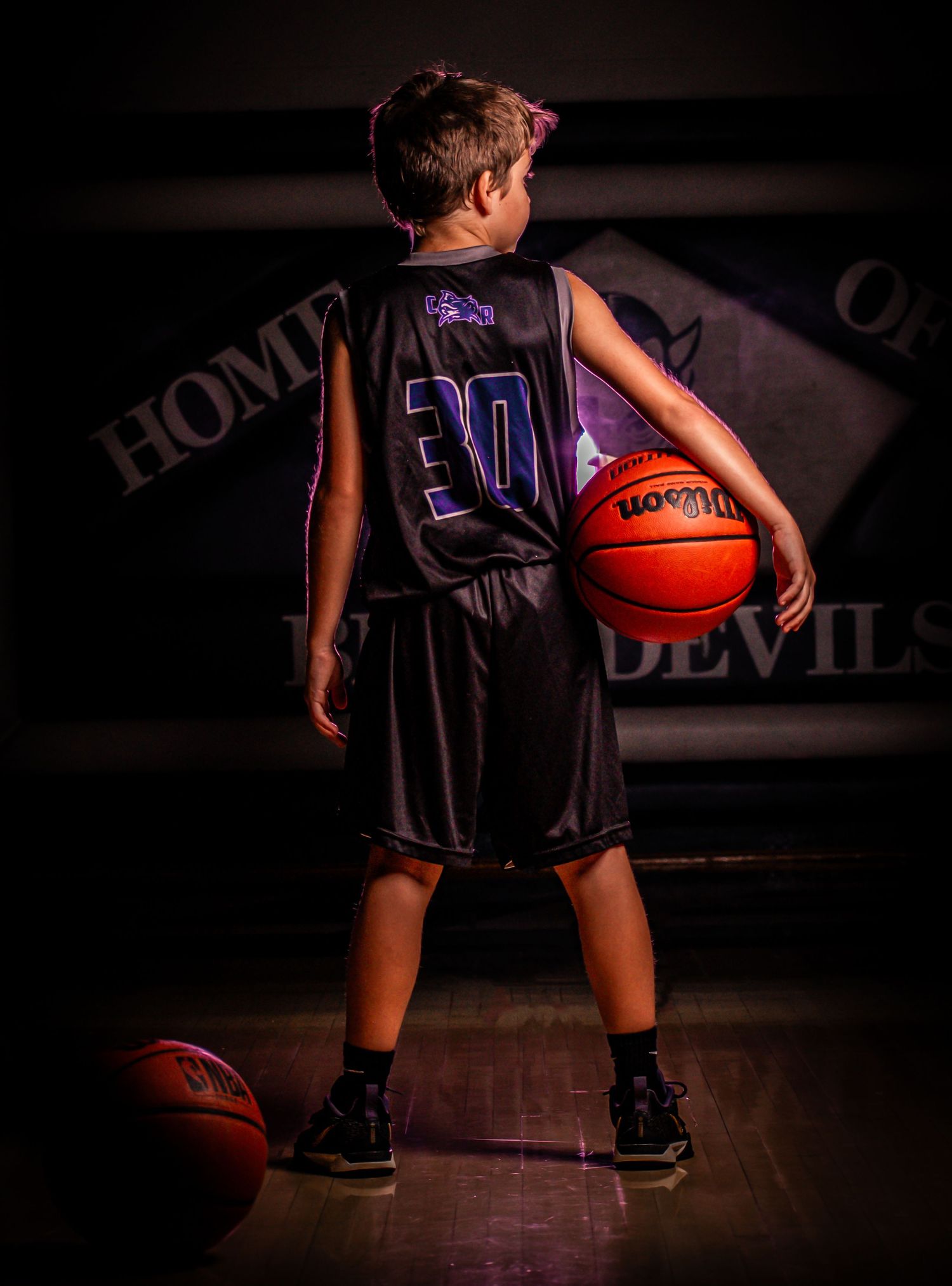 Basketball player in purple jersey number 30 dribbles ball on dark court with dramatic lighting effect.