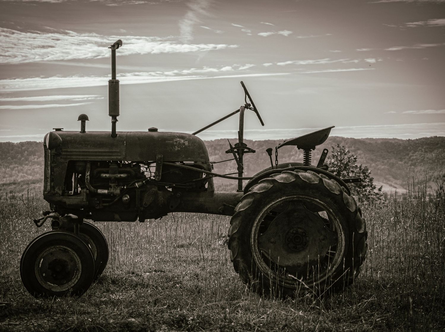 A vintage tractor silhouetted against a dramatic sky in black and white photography.