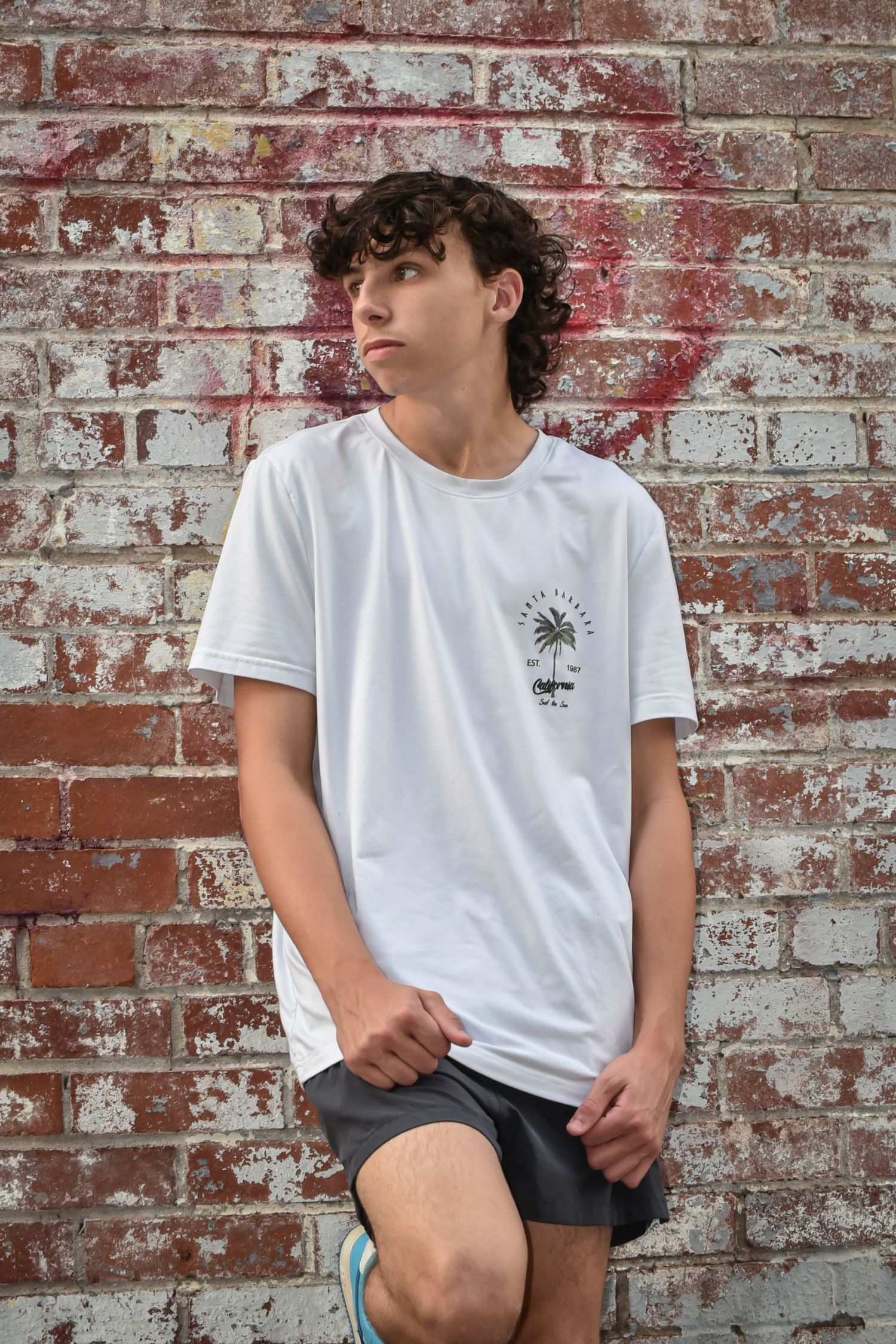 Fashion portrait against weathered brick wall wearing white graphic tee.