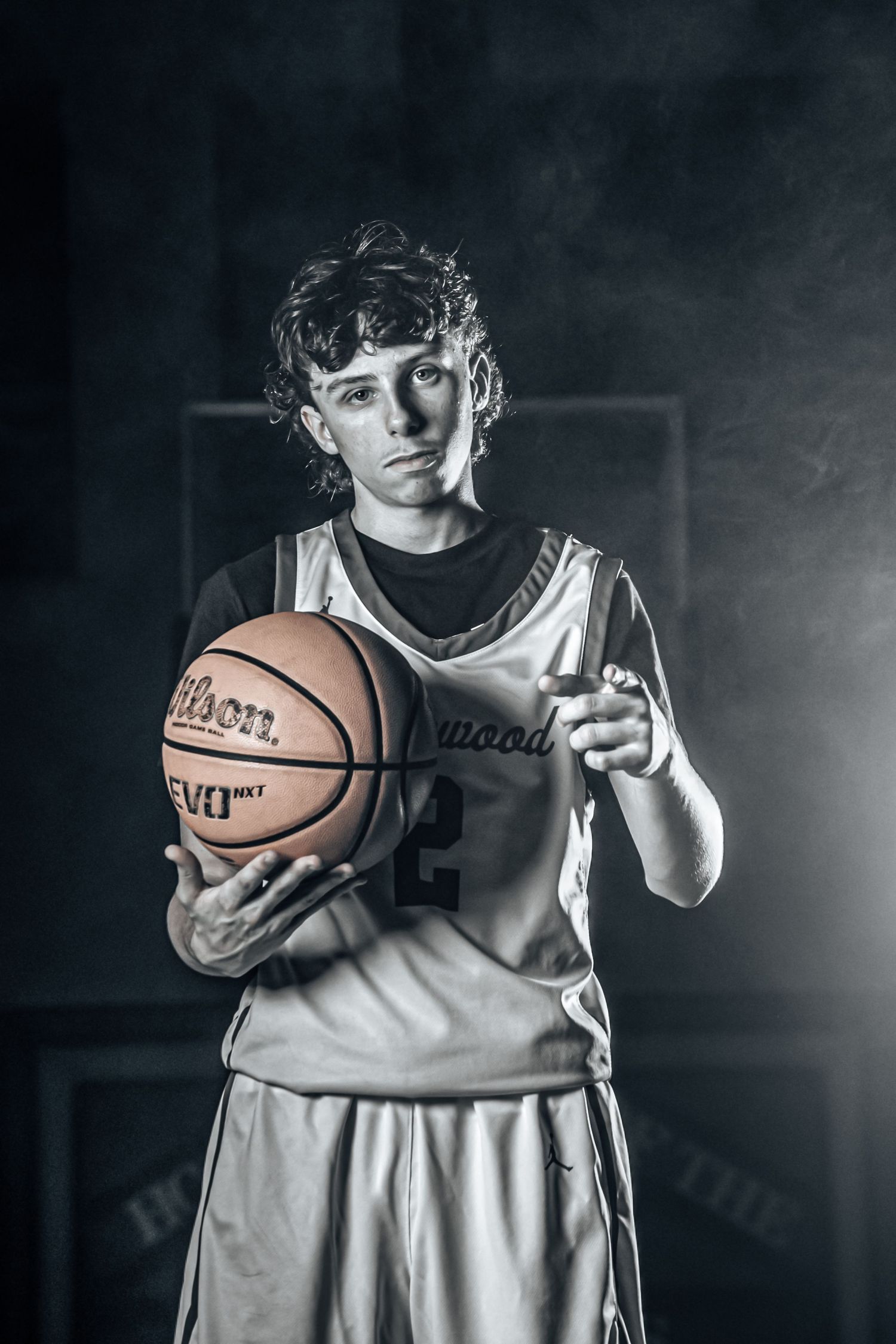 Basketball player in white uniform poses with ball against moody dark background.