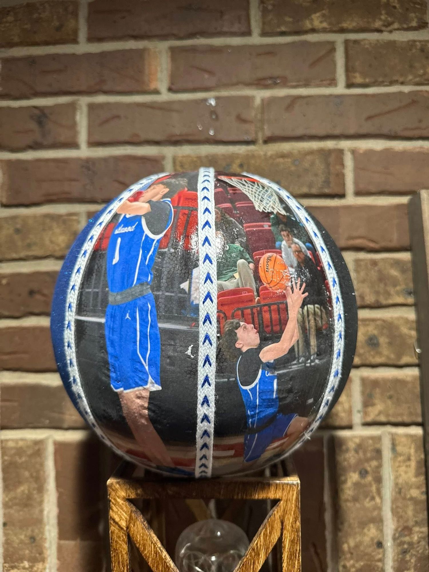 Painted basketball with artistic designs displayed on wooden stand against brick wall.