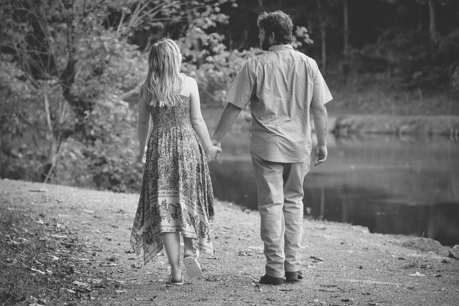 A black and white photo of two people walking along a lakeside path.