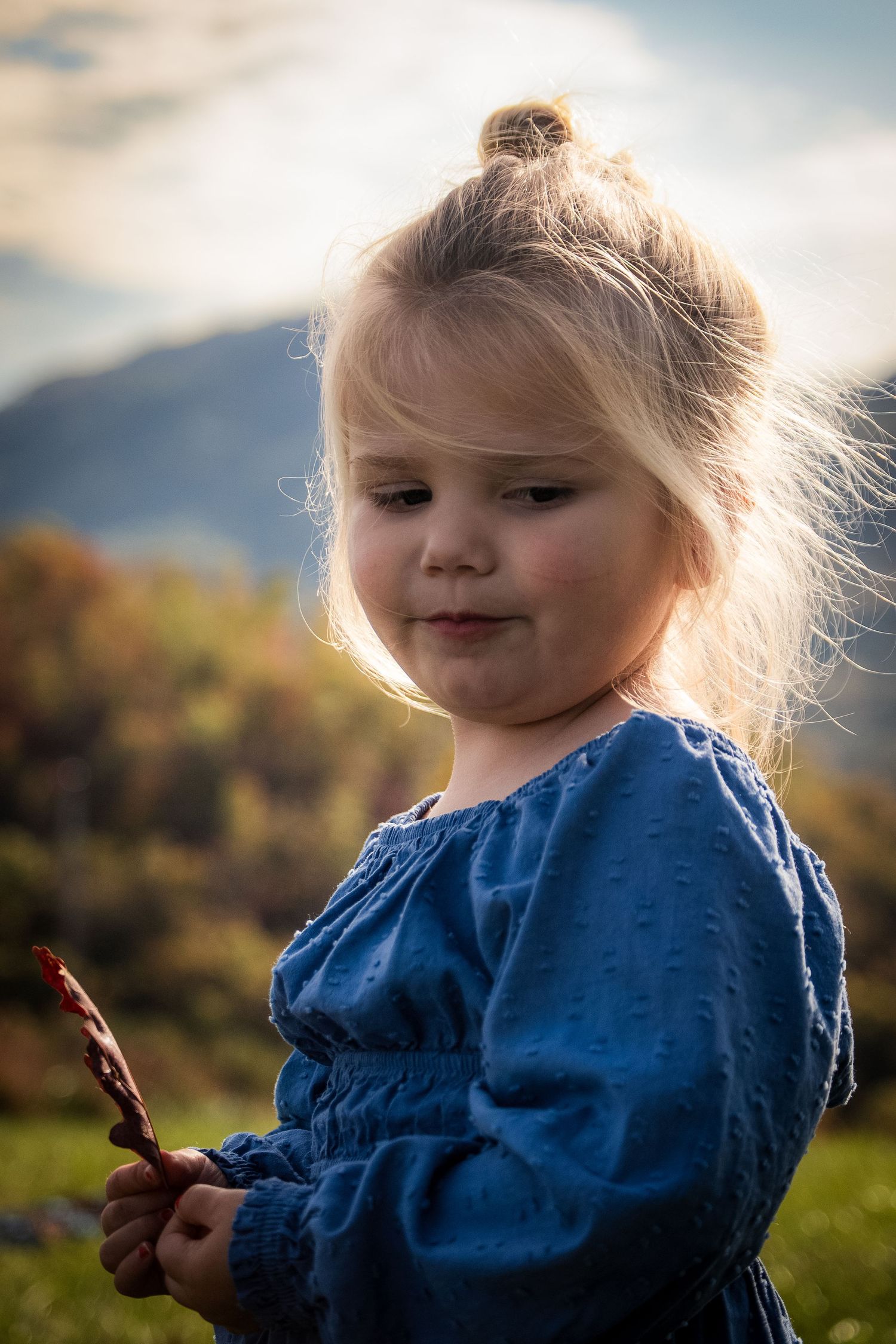 Sunlit portrait of child in blue dress enjoying outdoor playtime.