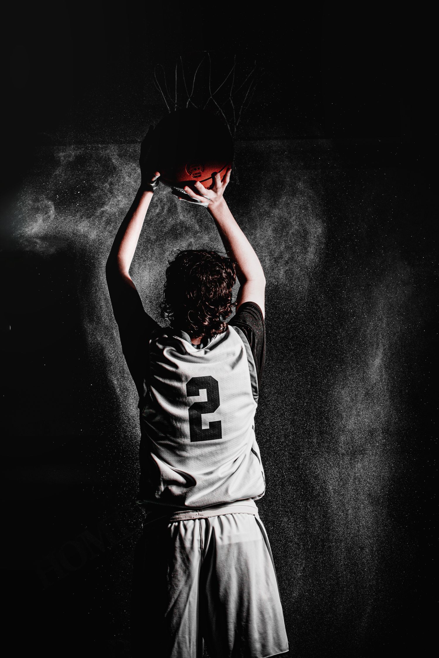Basketball player wearing jersey number 2 holds red ball against dark background.