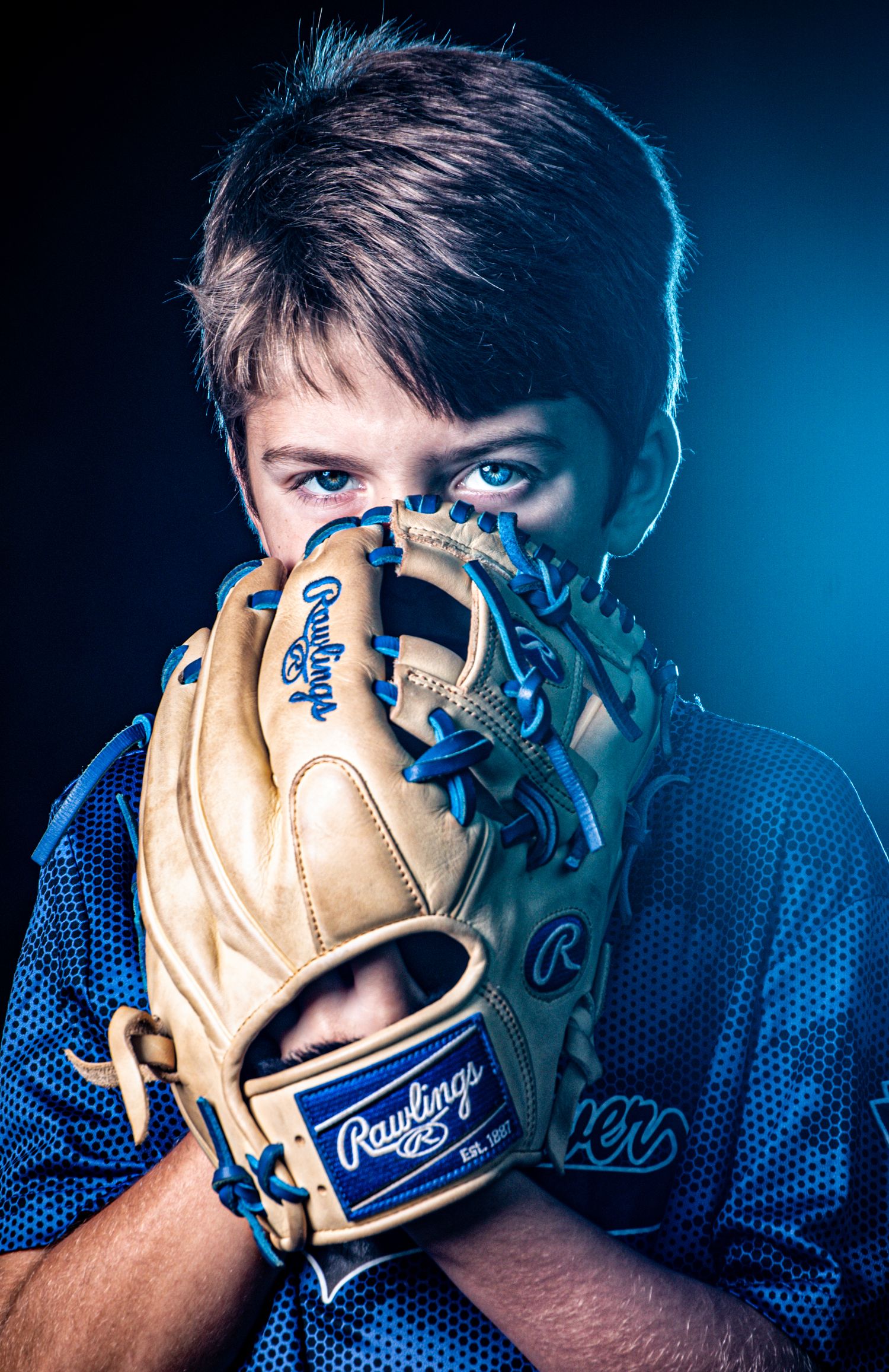 Baseball player poses with a tan Rawlings glove in dramatic blue lighting for a sports portrait series.