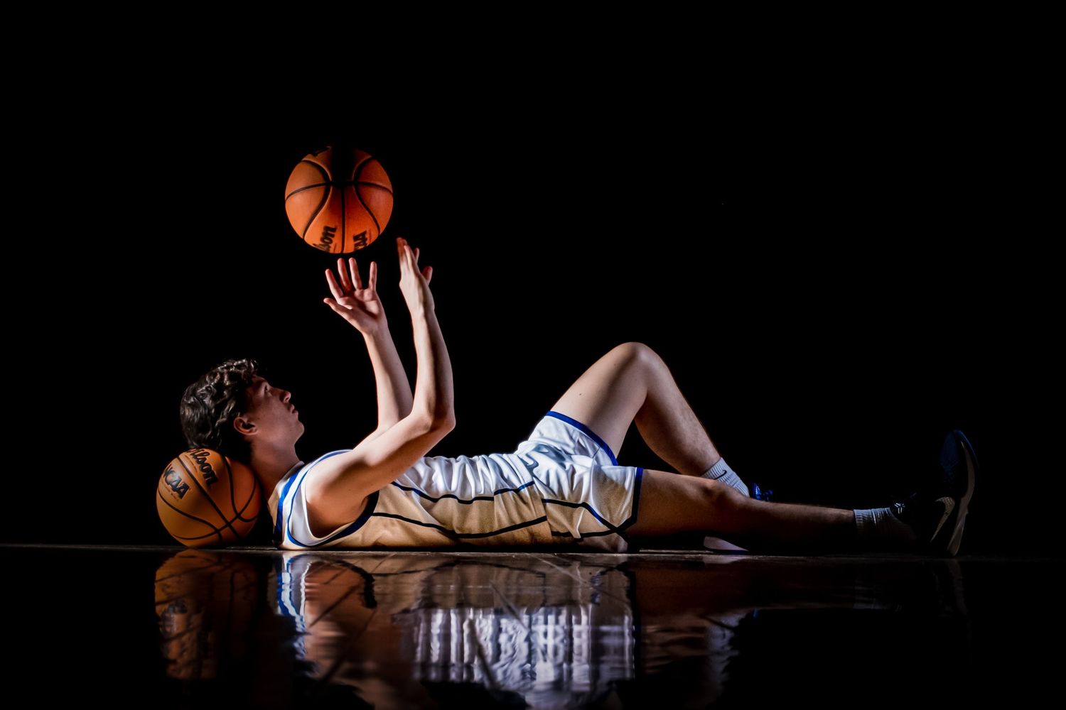 Basketball player lying on wooden floor with ball in artistic lighting.
